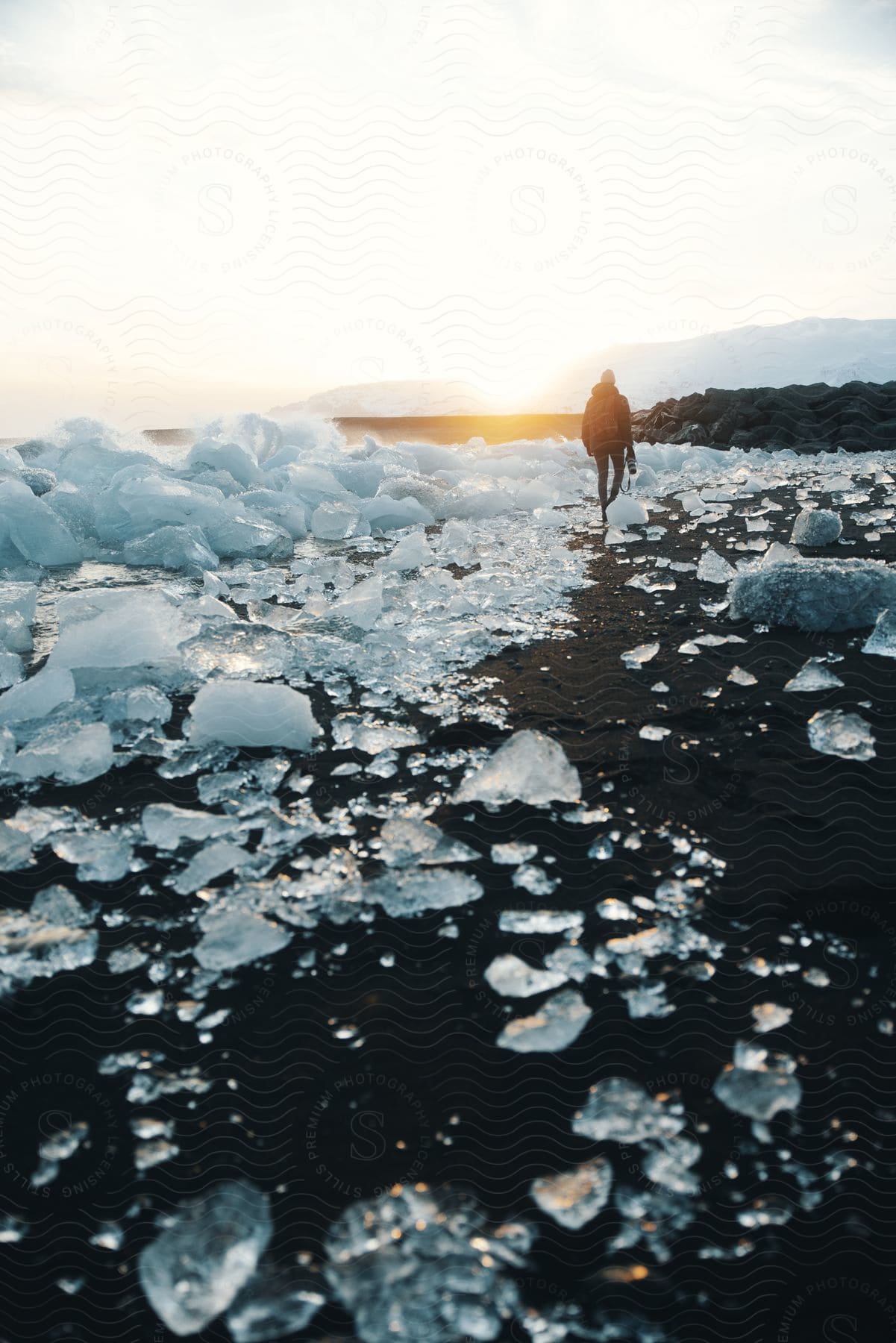 A person walking on a snowy beach with mountains and the sea in the background