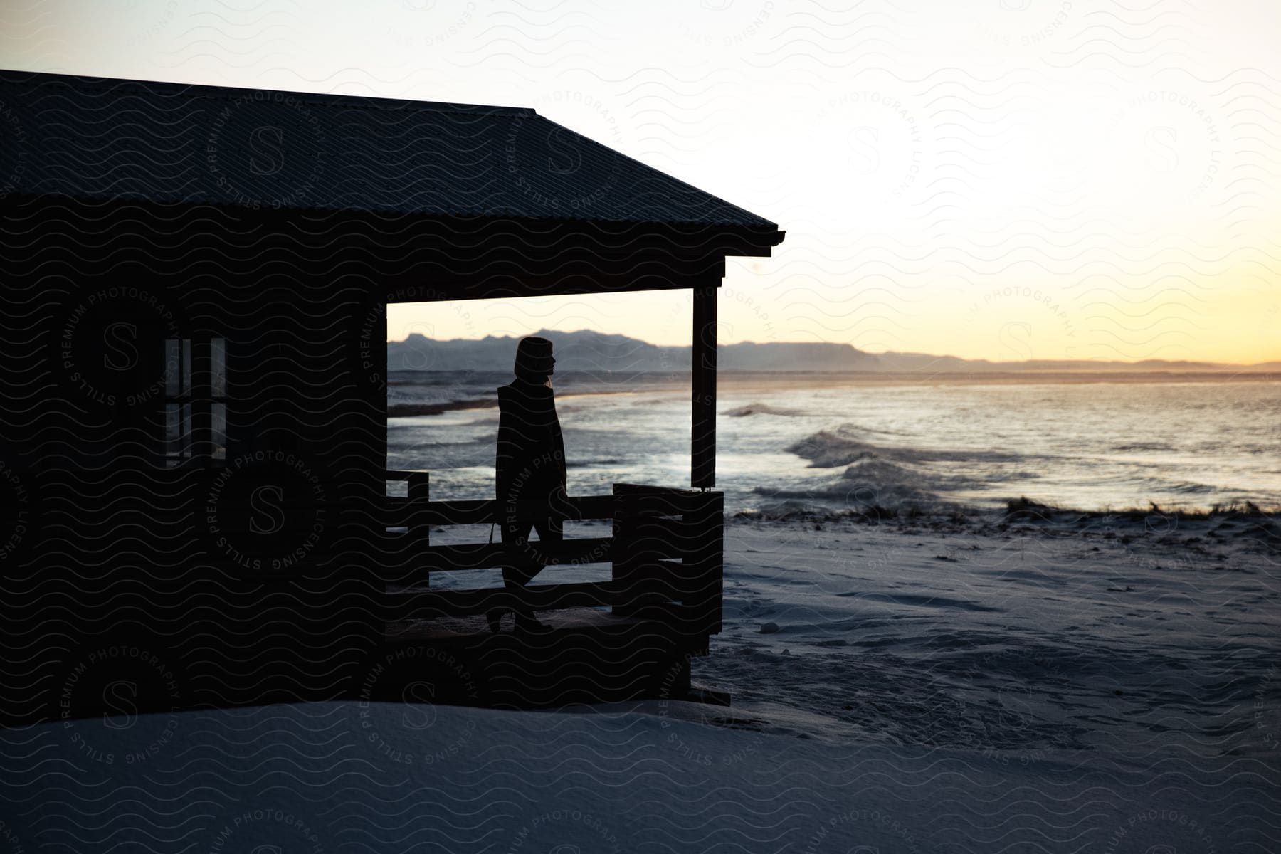 Silhouette of a woman looking at the ocean from a waterfront house at sunset