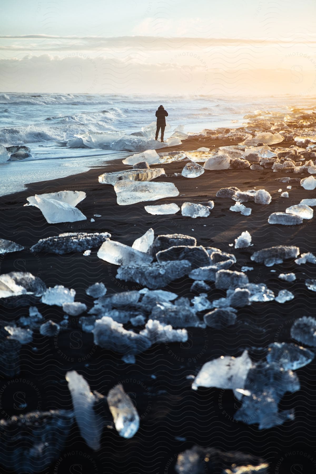 A man on the shore photographing the sea and the ice on the sand