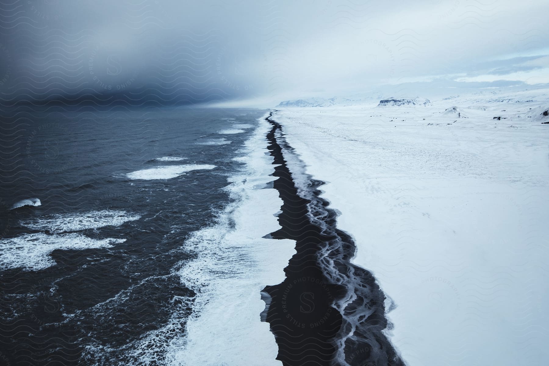 A frozen shoreline with icy waters and a snowy slope under a cloudy sky