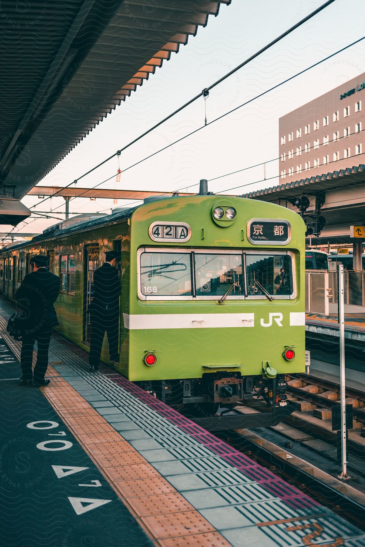 A green train stopped at the railway station with two men on board