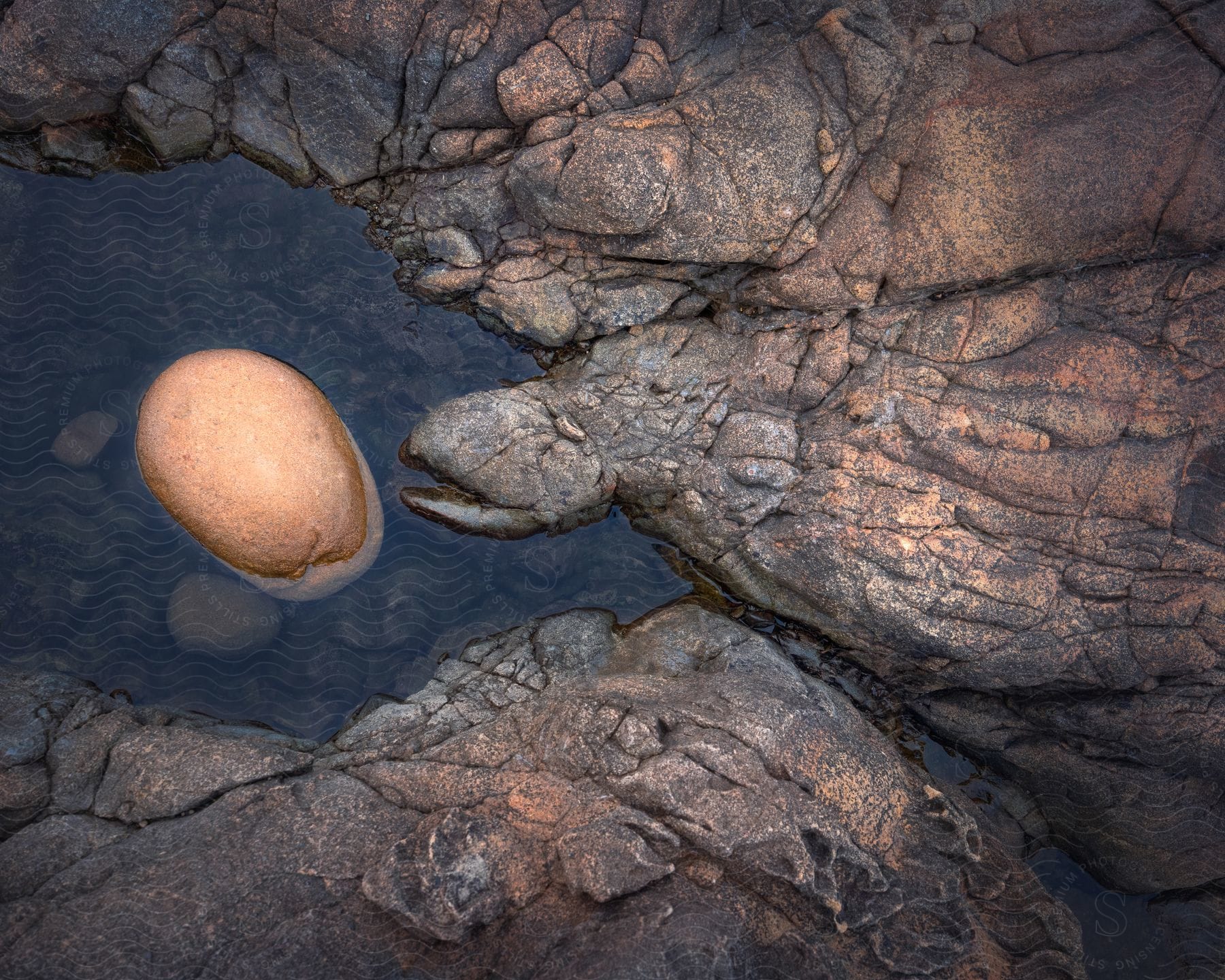 Rocky terrain with a small body of water resembling a lake and a massive rock in the shape of an egg with water cascading down gracefully