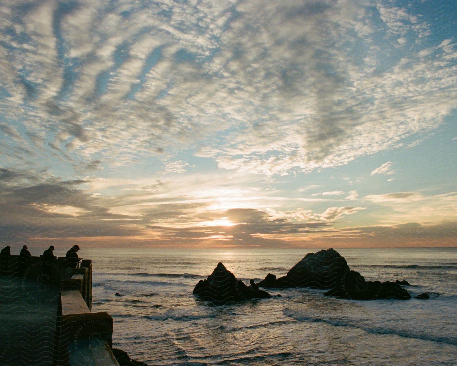 Coastline with rock mountain in the middle of the sea and people watching the sunset