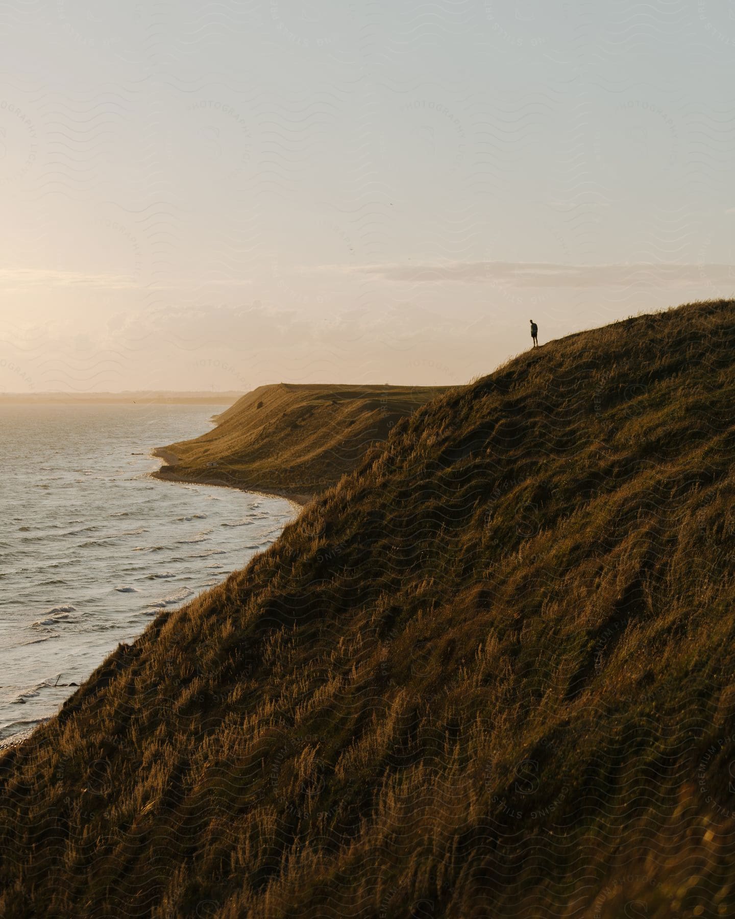 Stock photo of silhouette of a person standing on top of a promontory with waves rolling into shore