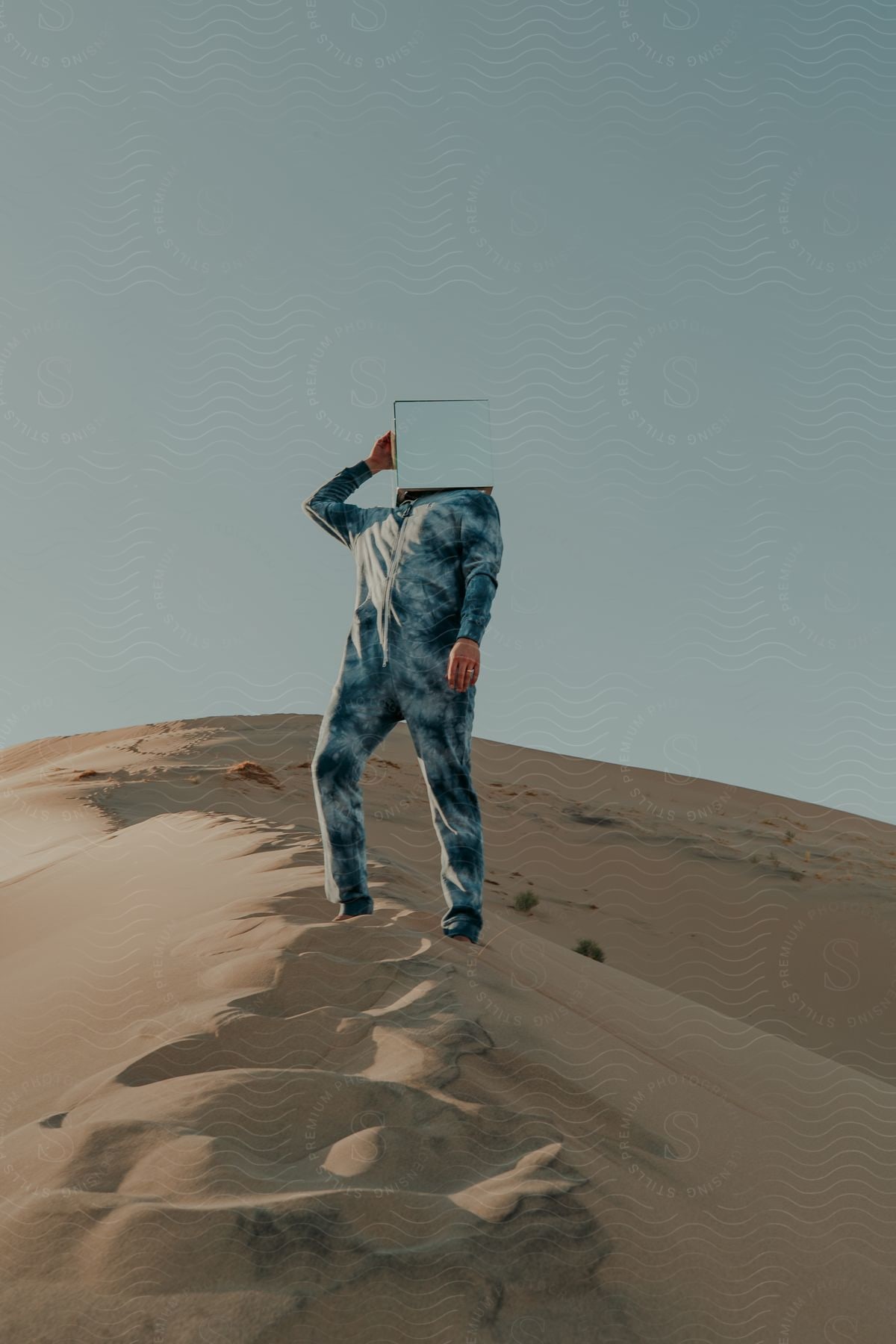 A man stands in the desert with a mirrored box on his head