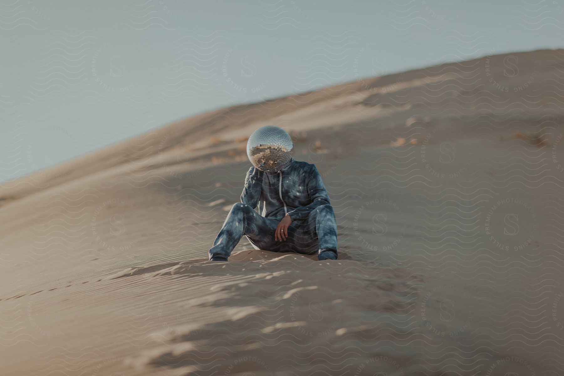 Stock photo of person with a mirror ball on their head sitting on a sand dune in the desert at dusk or dawn