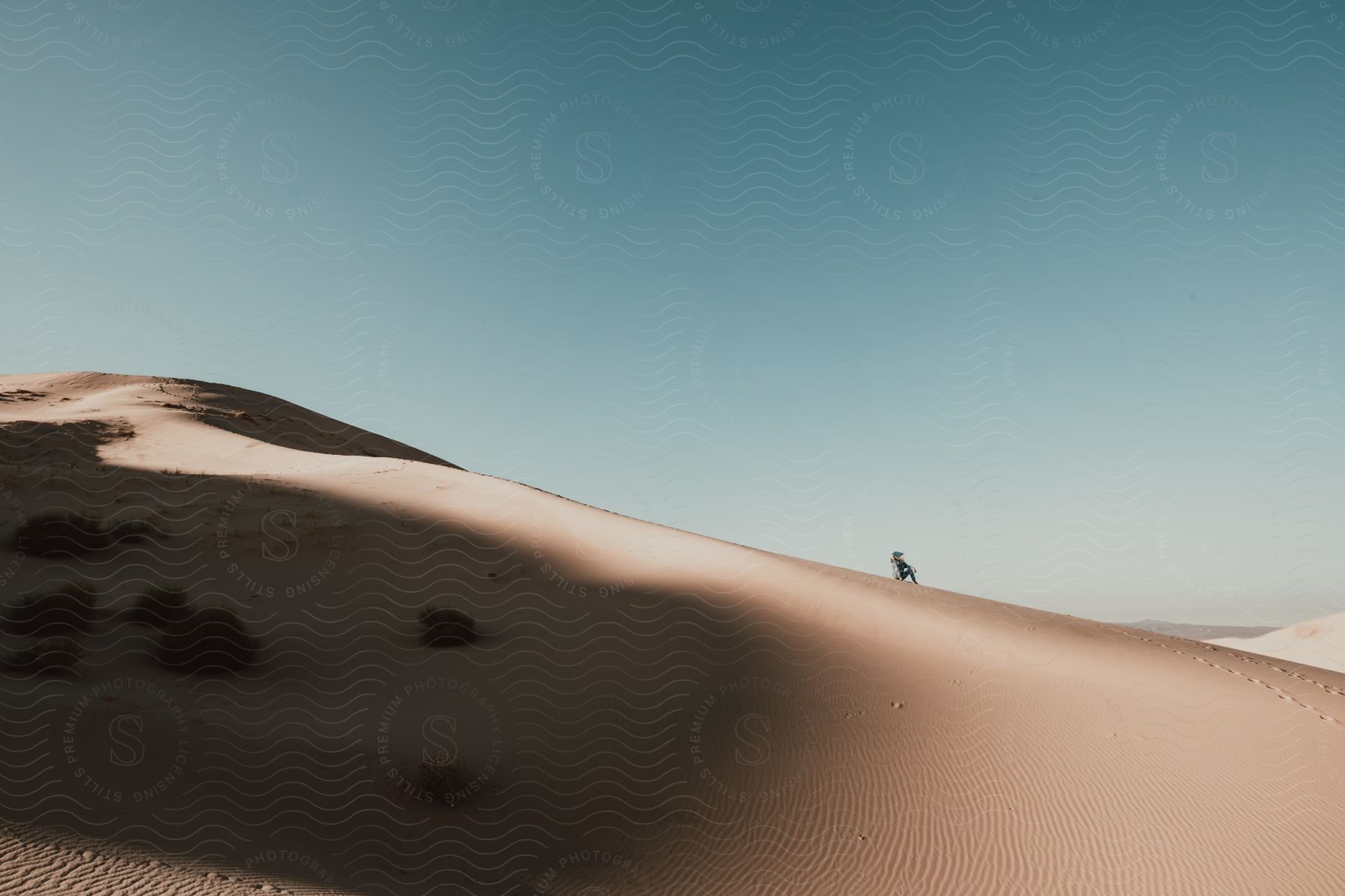 Man sitting on sand dune wearing spacesuit visor reflects vast desert landscape