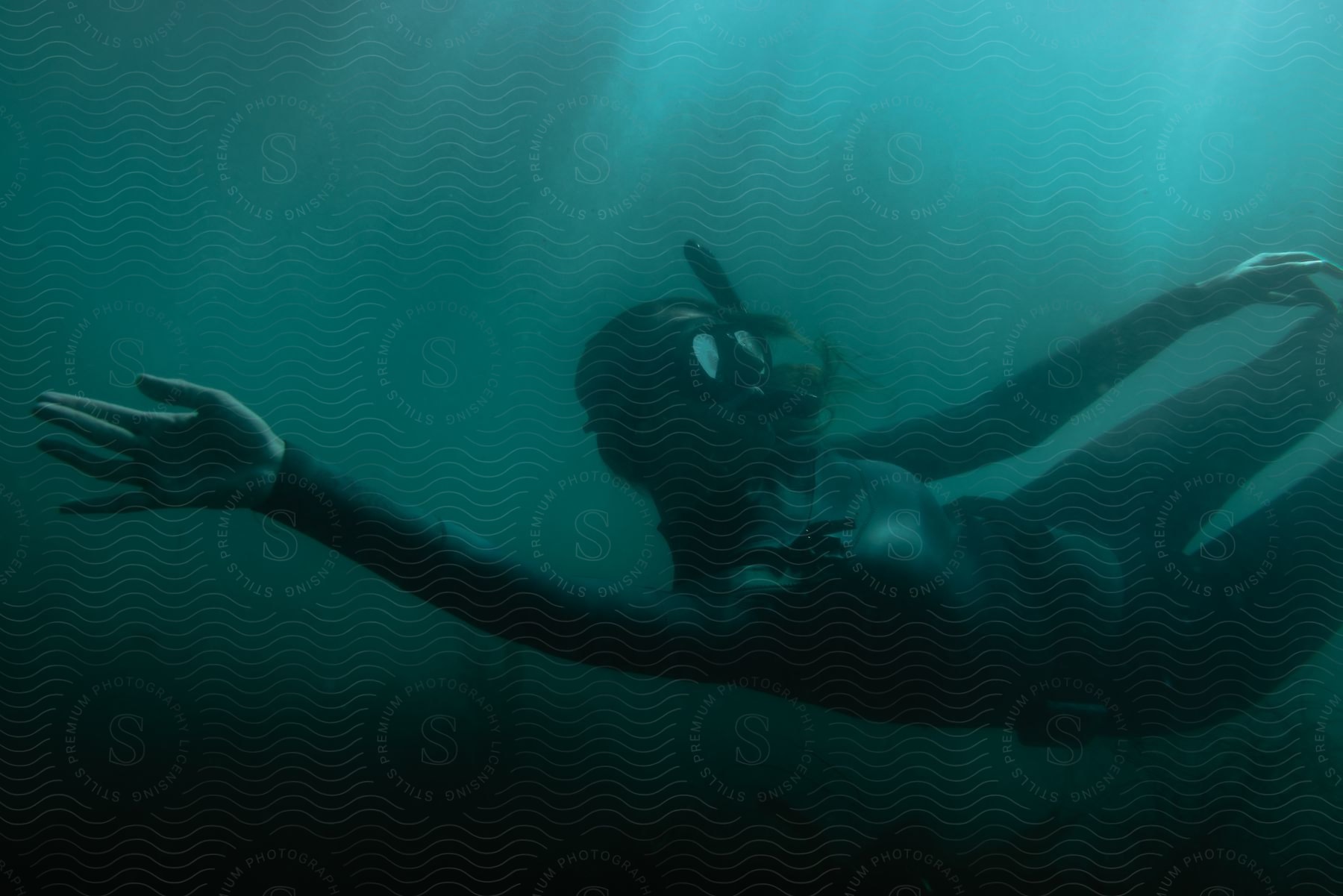 A woman in a wet suit with a snorkel on swimming underwater