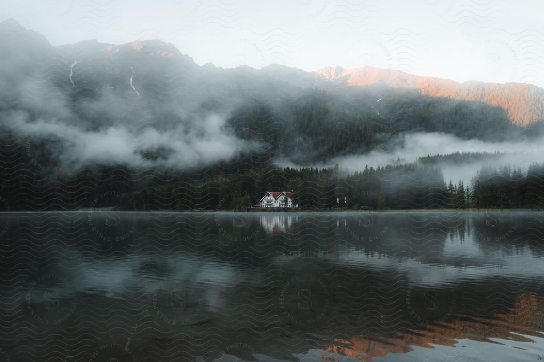 Foggy forest with white house near lake reflecting landscape