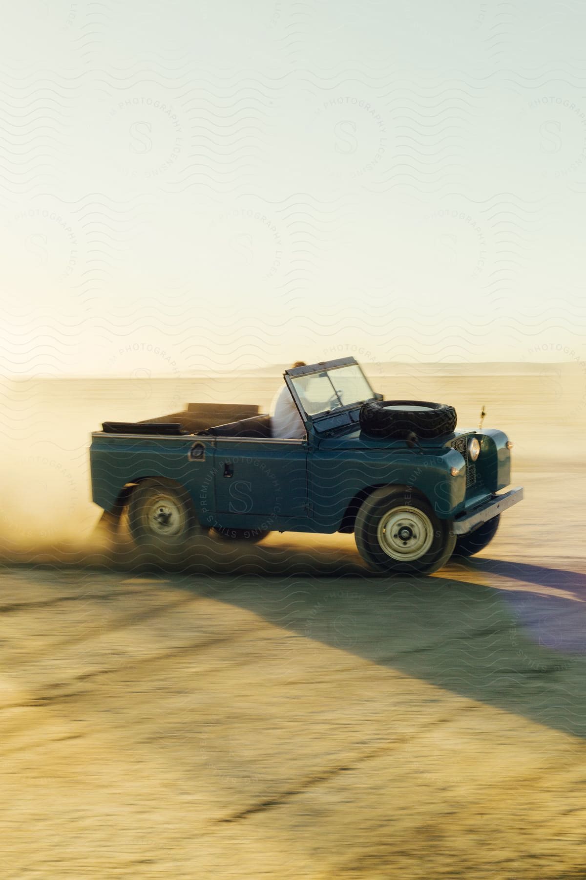 An old vehicle driving on a desert plain with dust being blown up from the moving vehicle