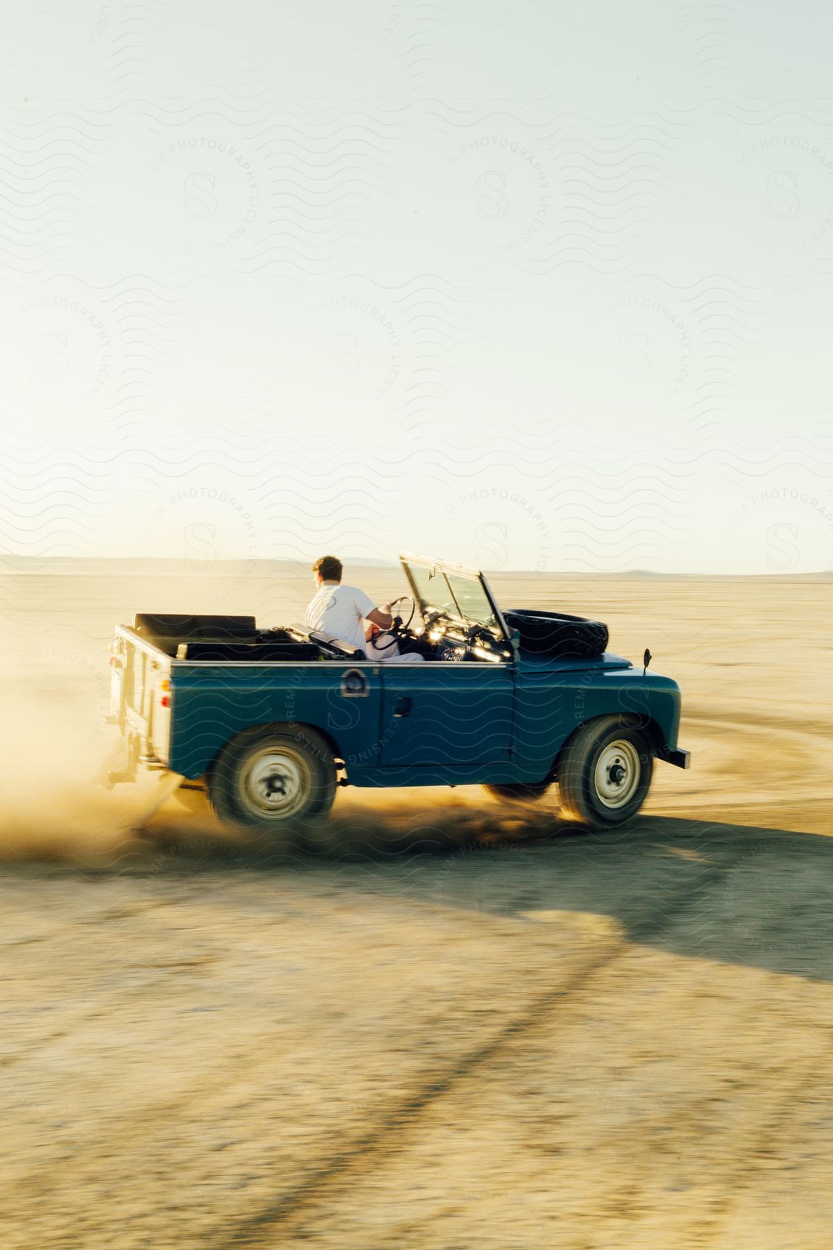 Blue convertible jeep driving on desert sand kicking up dust on a sunny day