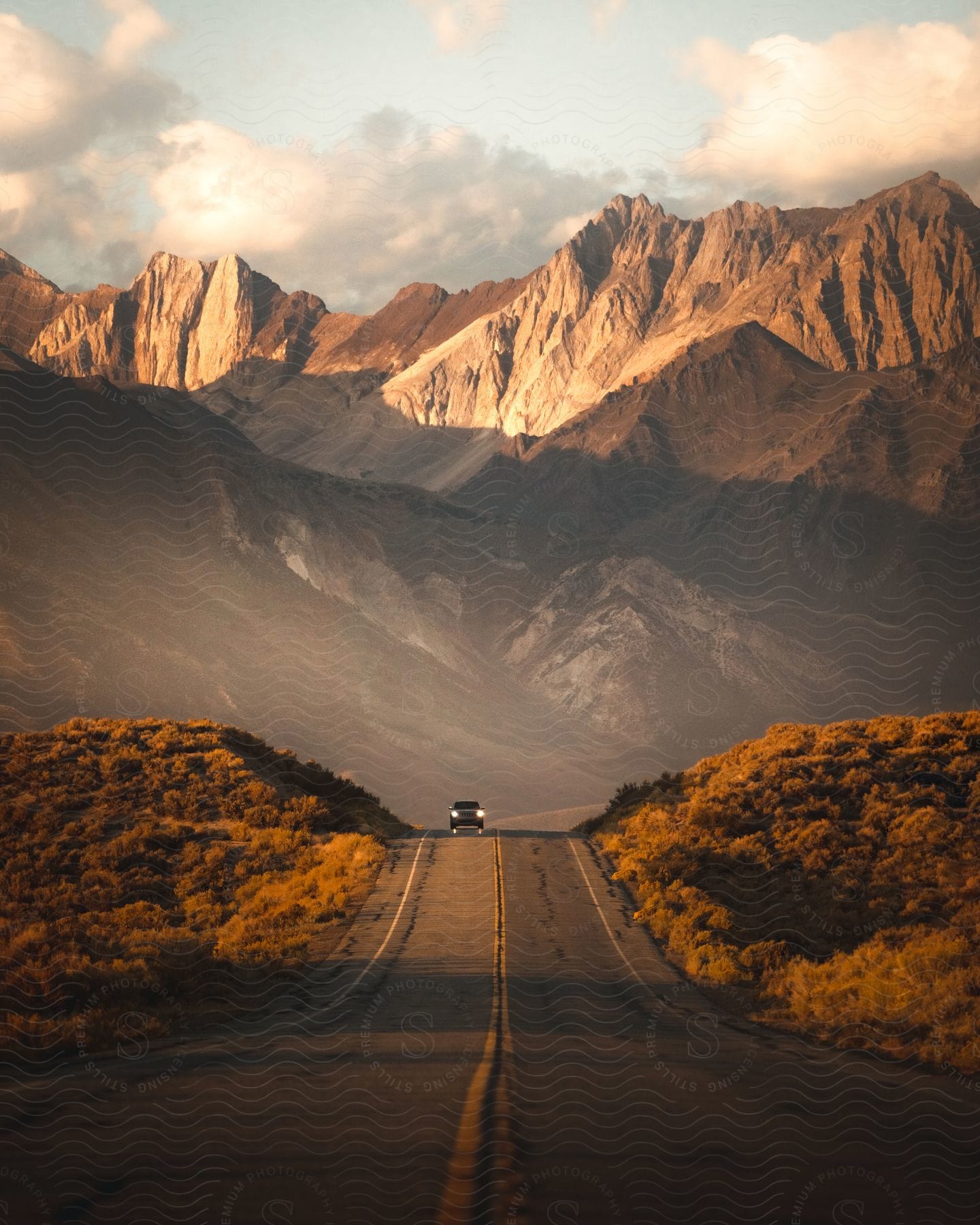 A car drives on a road with a mountain range in the background on a cloudy day