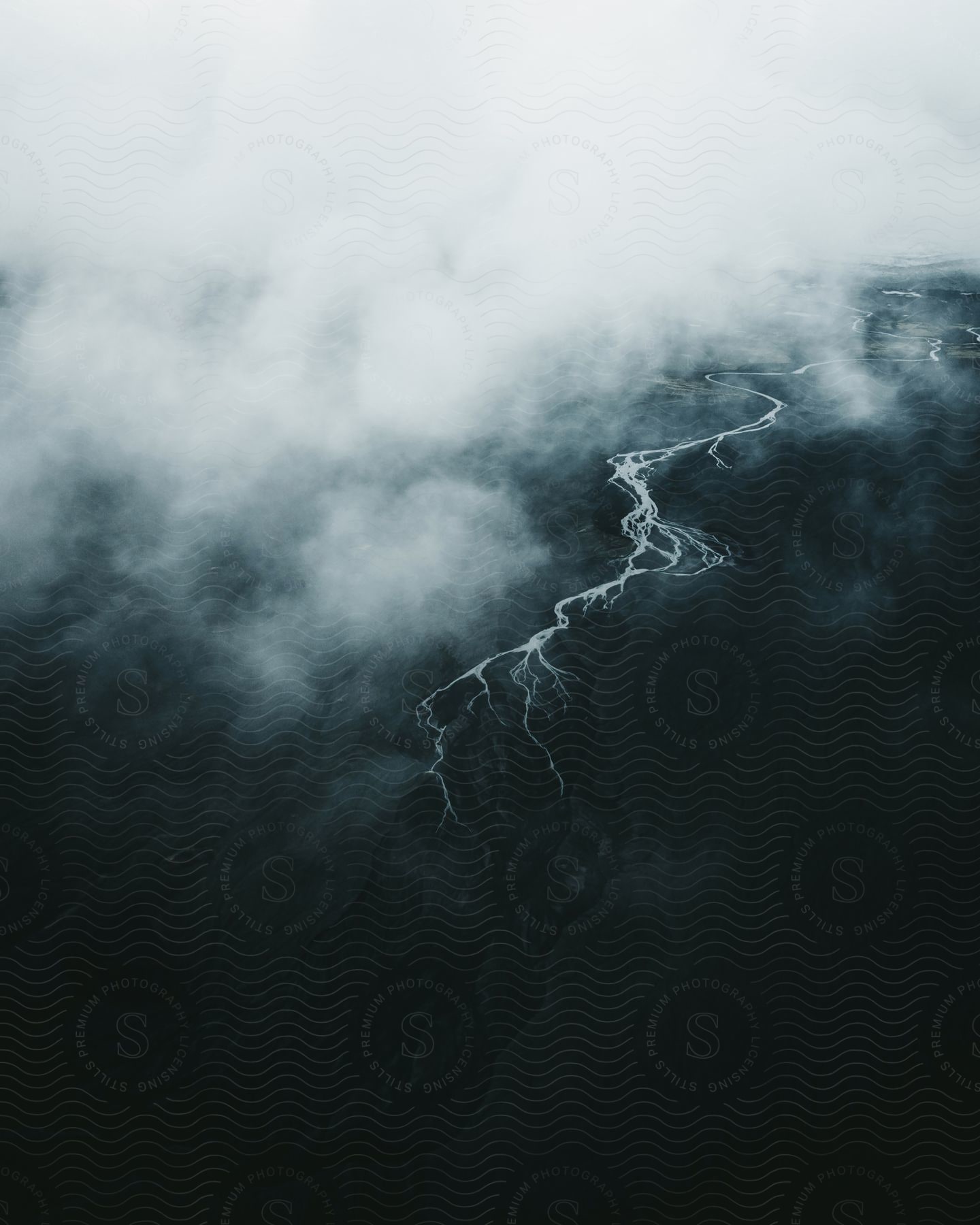 Aerial view of a river running through dark mountains with fog settling over the land