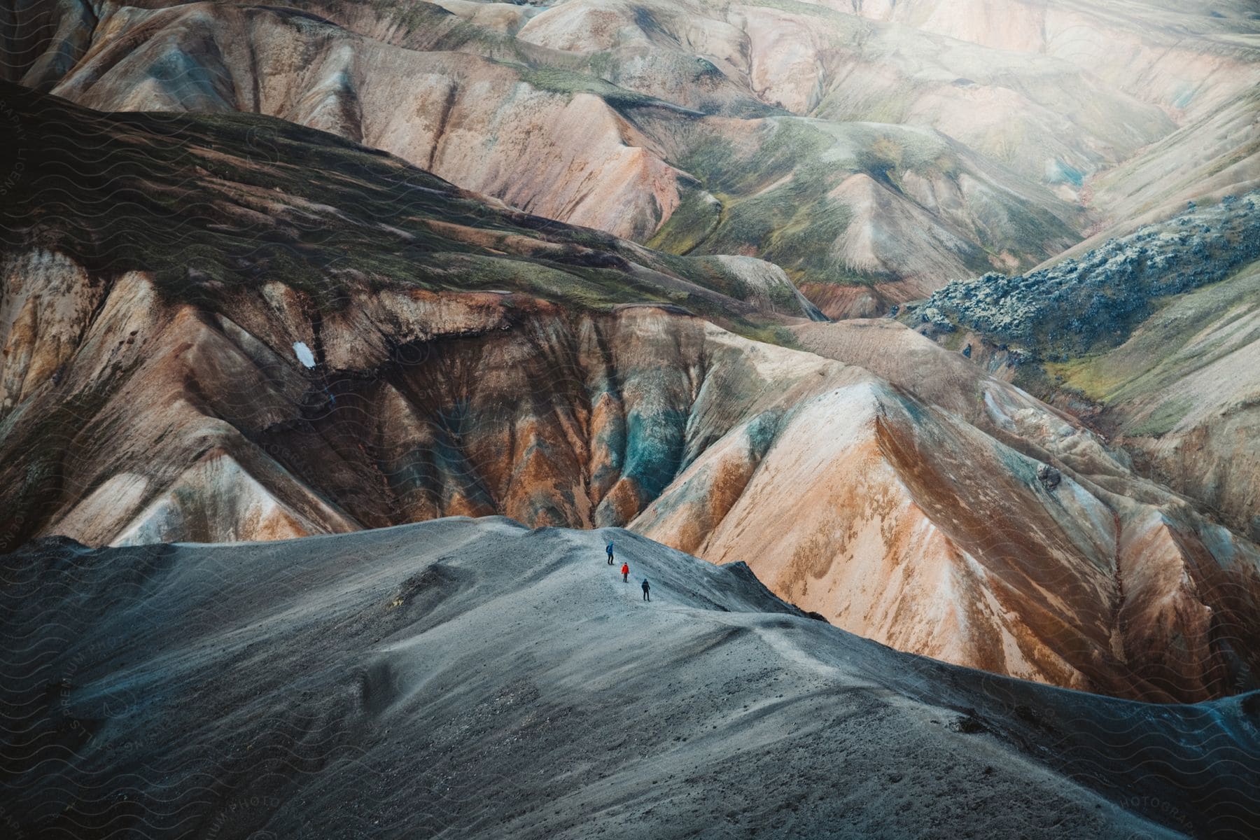 Three mountaineers walking over the ridge of a colorful mountain range from an aerial perspective