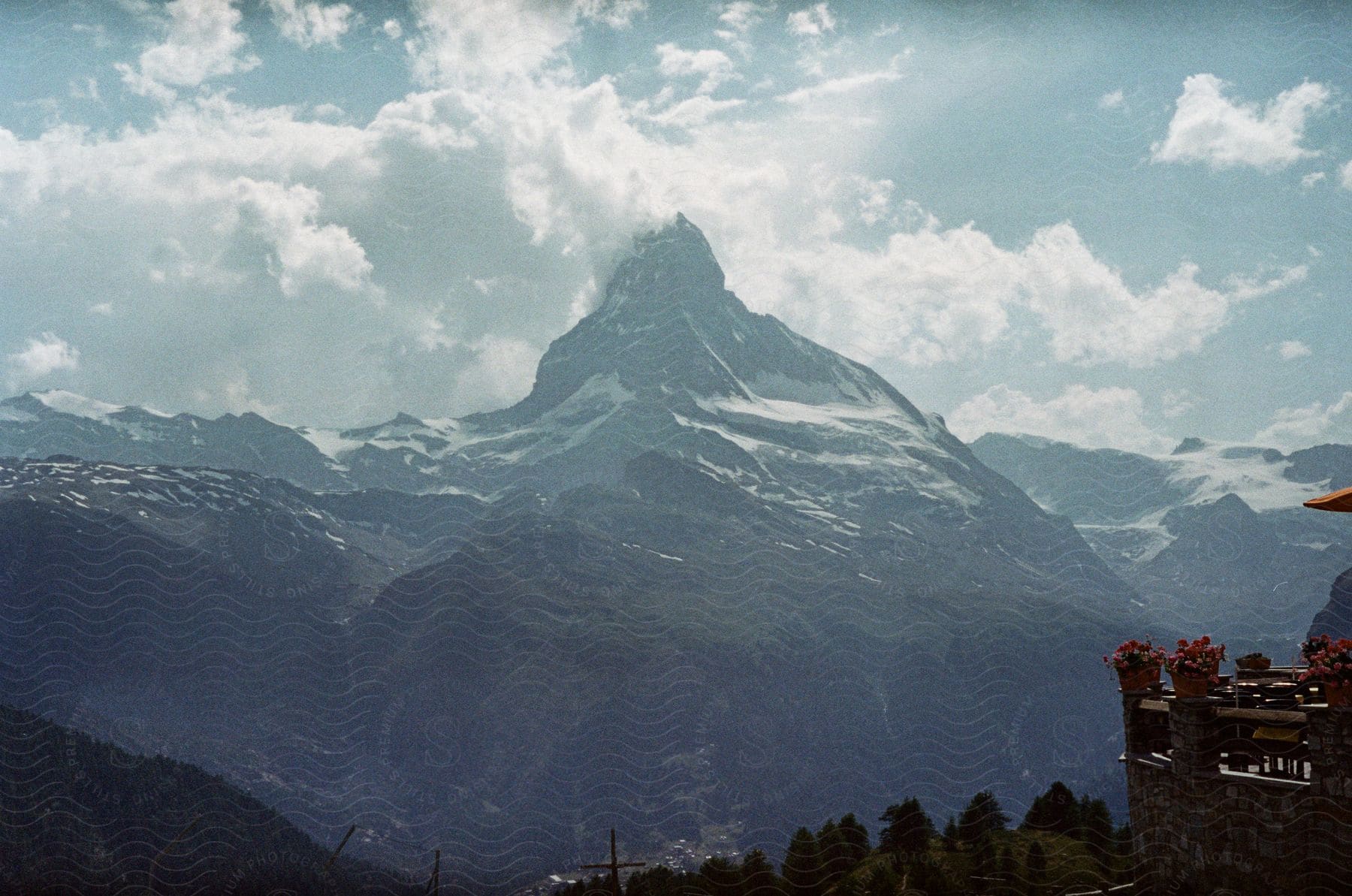 A Snowcovered Mountain With Peaks Under A Cloudy Sky With The Sun Shining Through