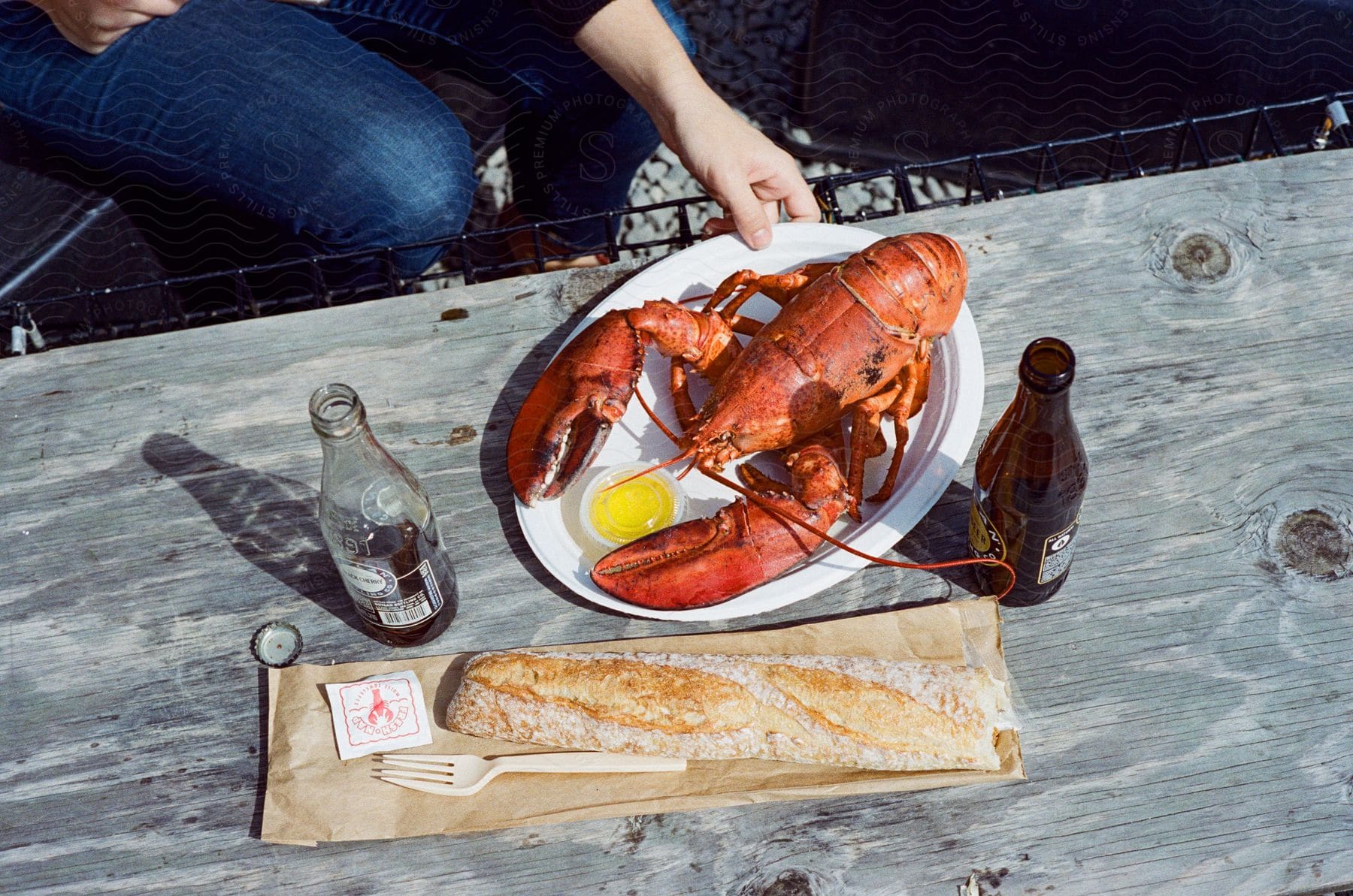 A wooden table displays an american lobster a beer bottle and a loaf of bread promising a satisfying meal