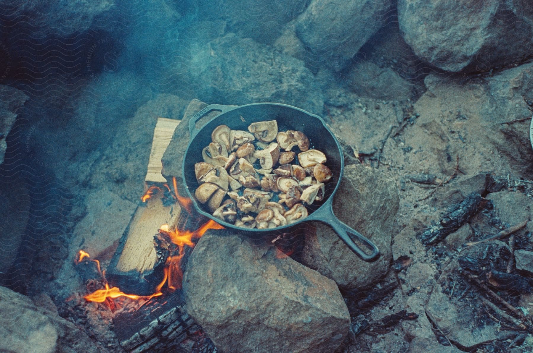 A meal being cooked on a castiron over a fire built in the wilderness over rocks