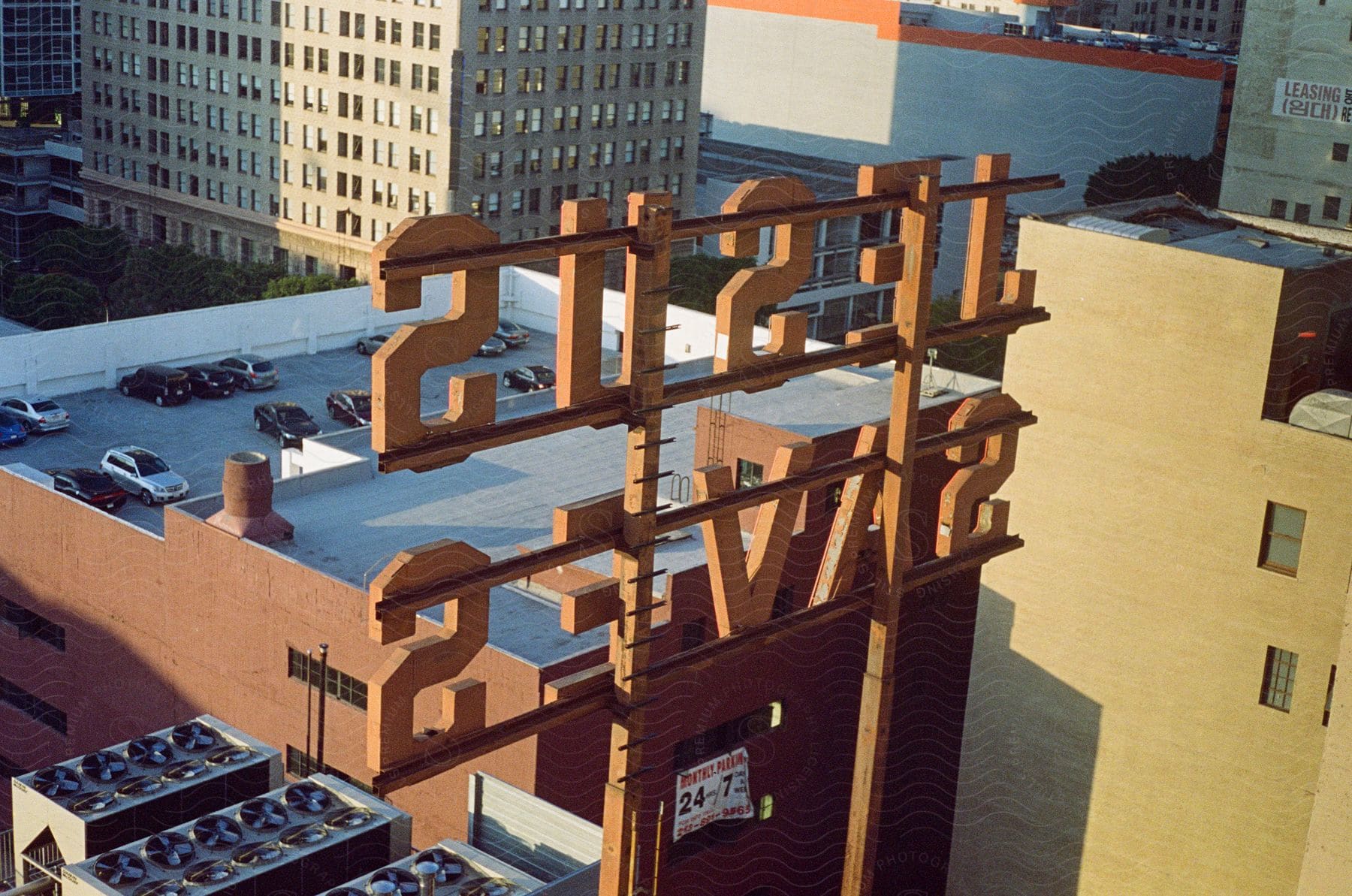 A city building overlook with a large sign and a parking lot on top surrounded by cars