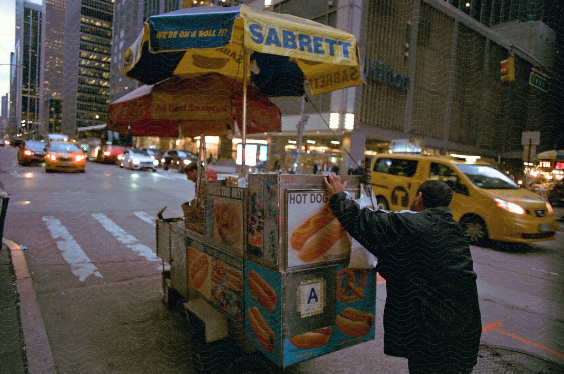 A man is pushing his food cart along the sidewalk on a busy road.