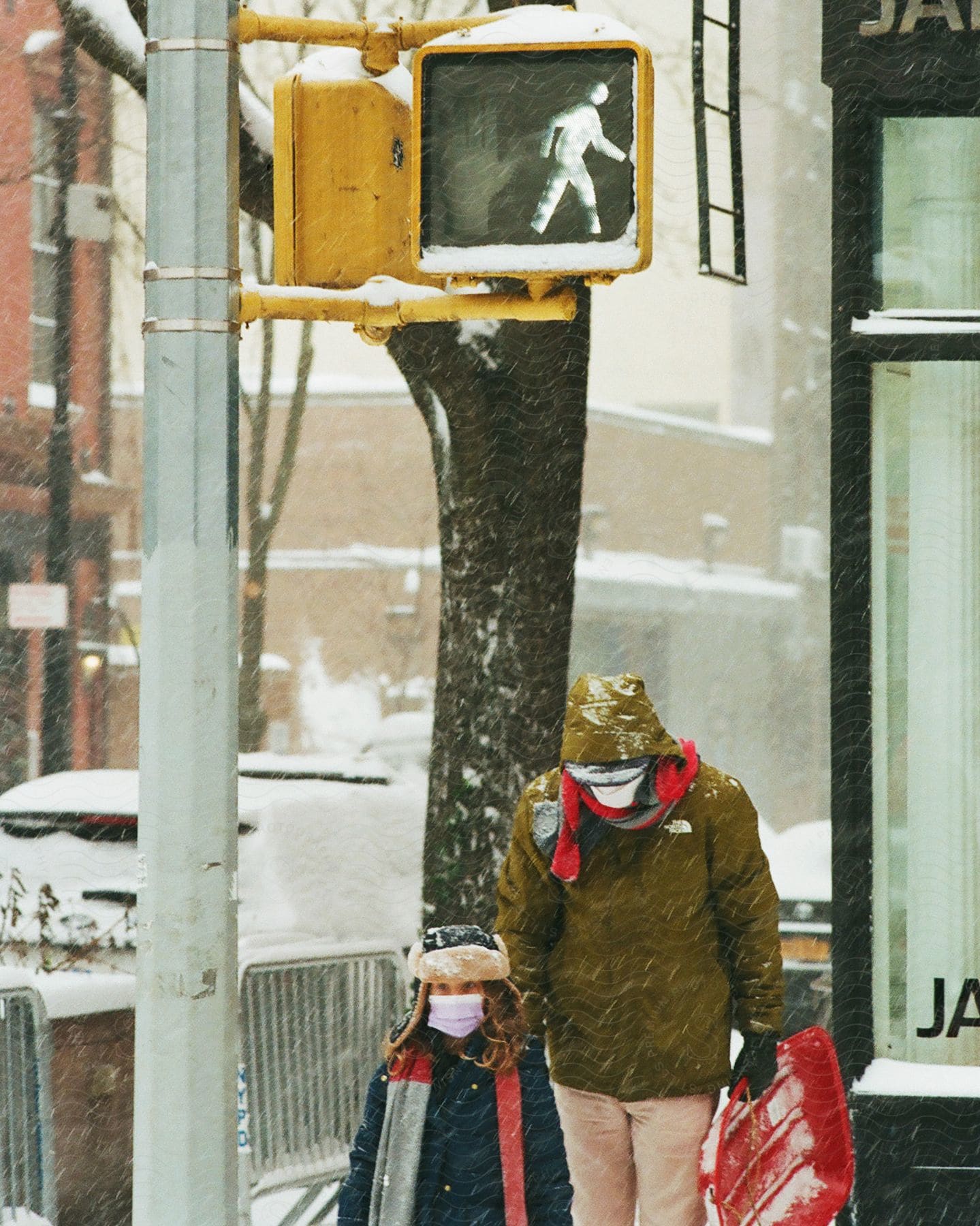 An adult and child are walking on the sidewalk during a snow storm.