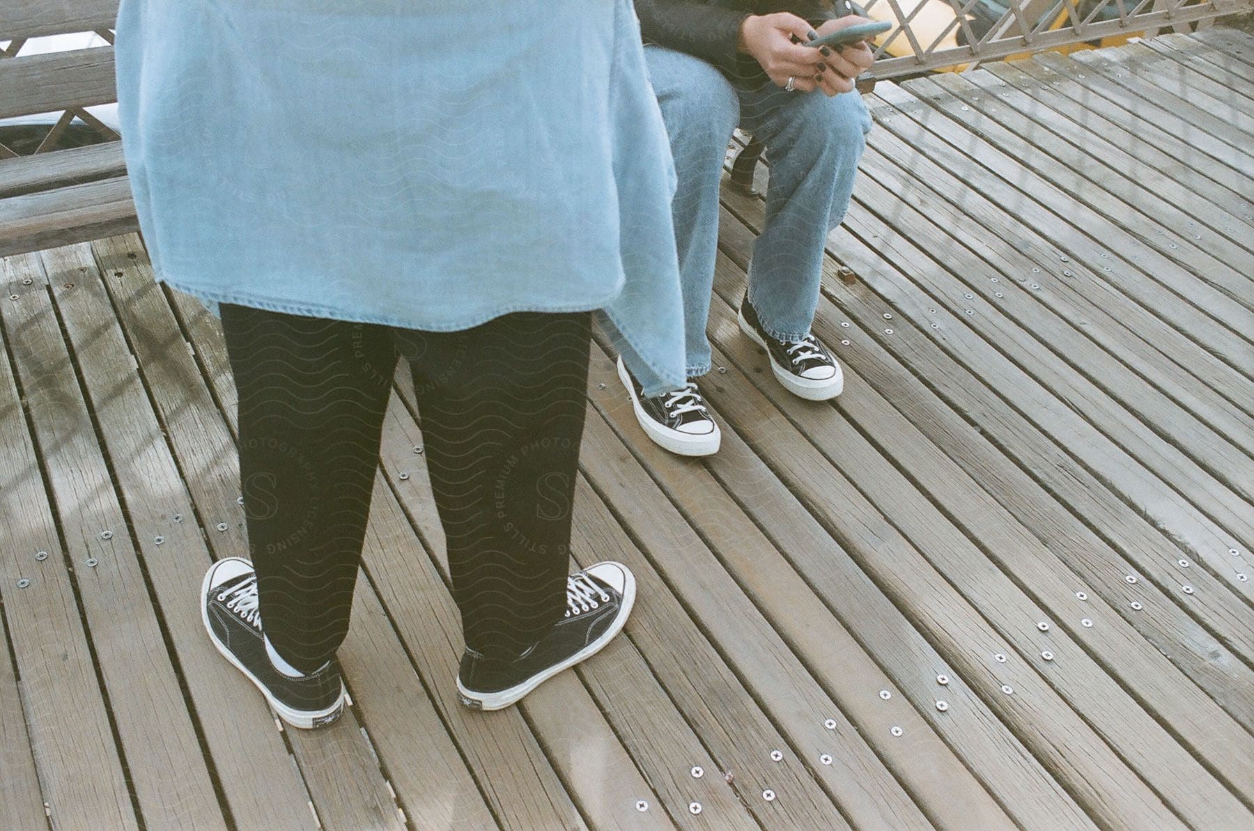 a couple of people standing on a wooden deck, using smartphone