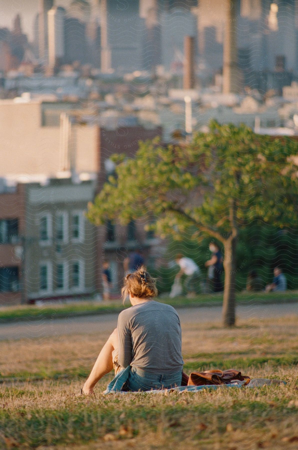 A woman looking sad sitting on a hill outside of a city.