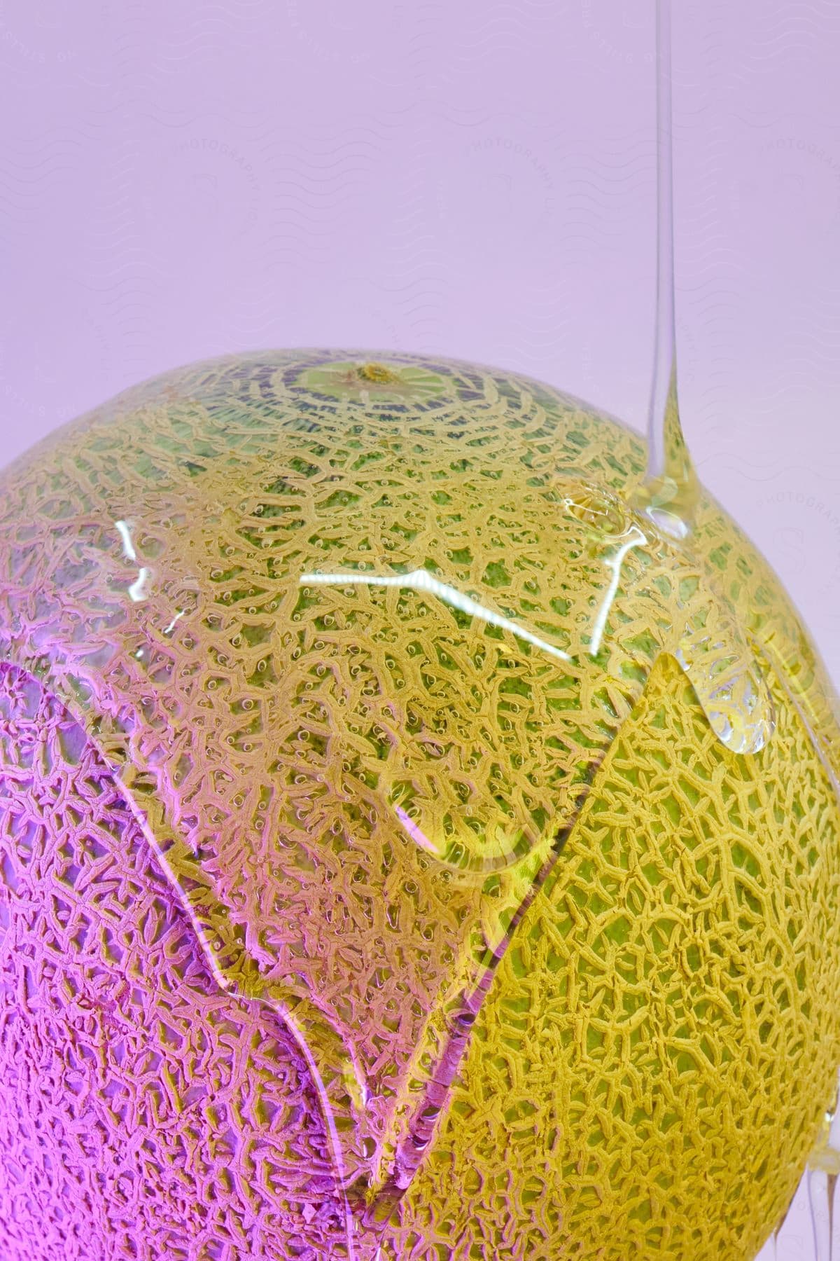 A cantaloupe is covered in a thick transparent liquid against a purple background