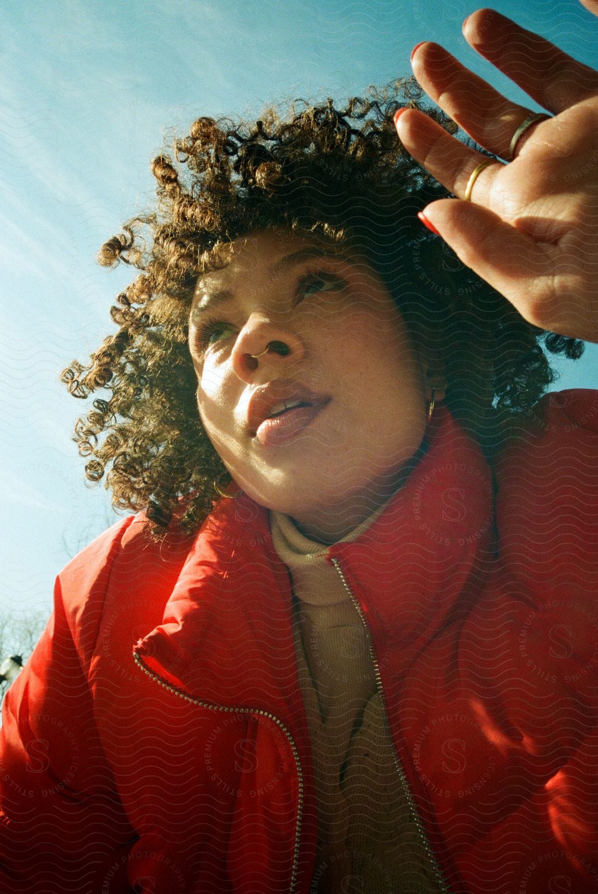 A woman wearing a puffy orange coat looks up with her hand next to her face