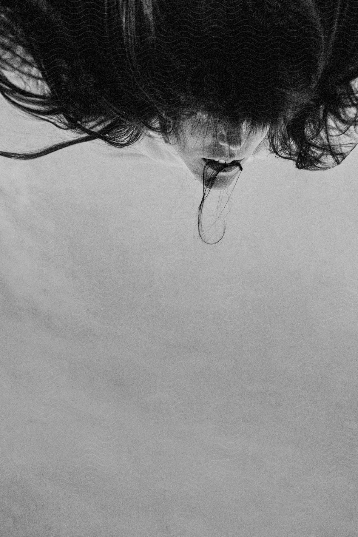 A captivating black and white portrait of a person with their face upside down hair falling into their mouth