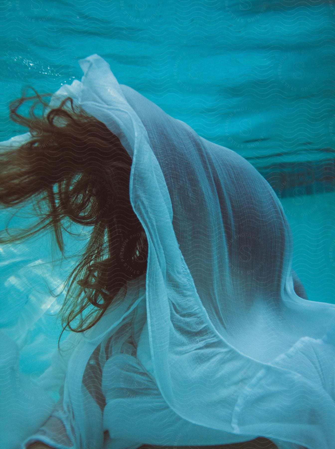 Redheaded woman underwater with hair and floating clothes covering her face