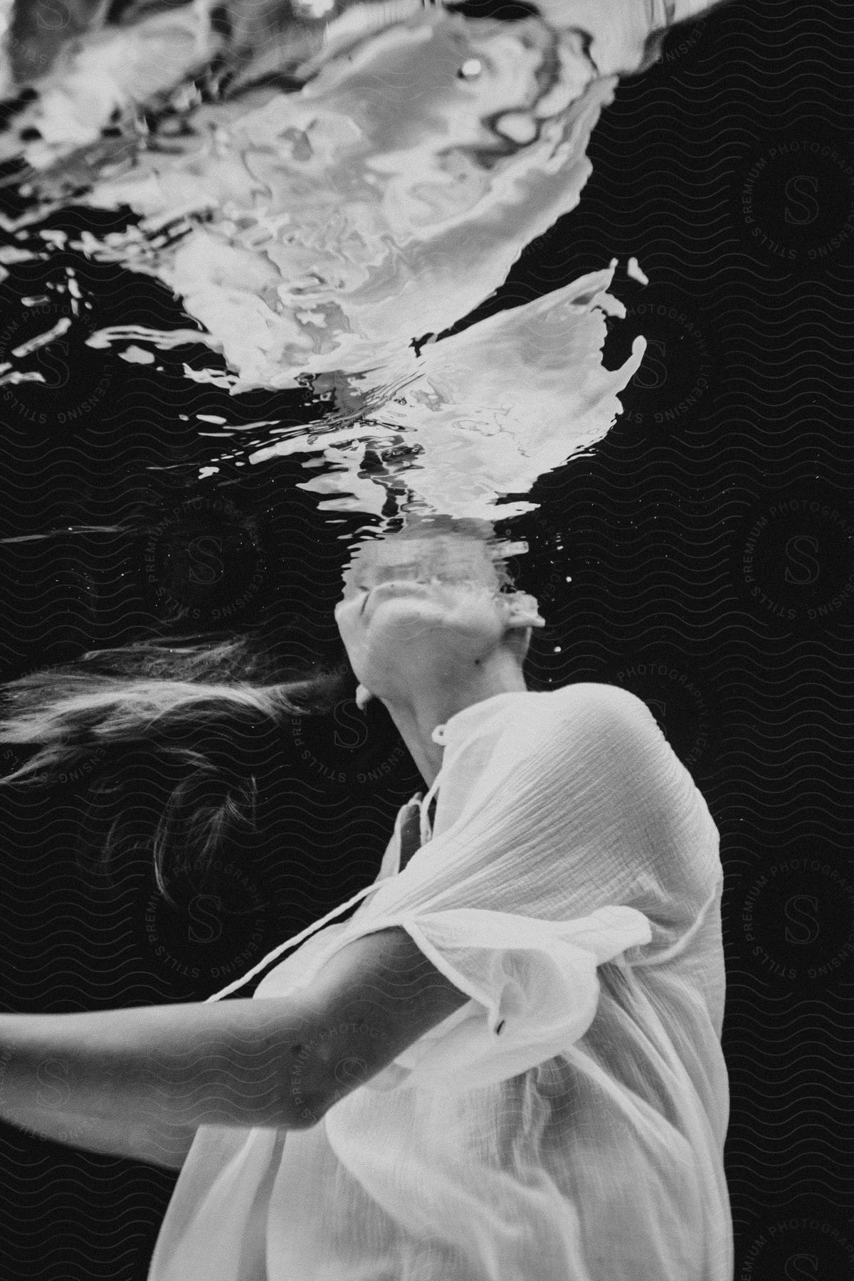 Woman wearing white underwater with distorted face reflection on water surface