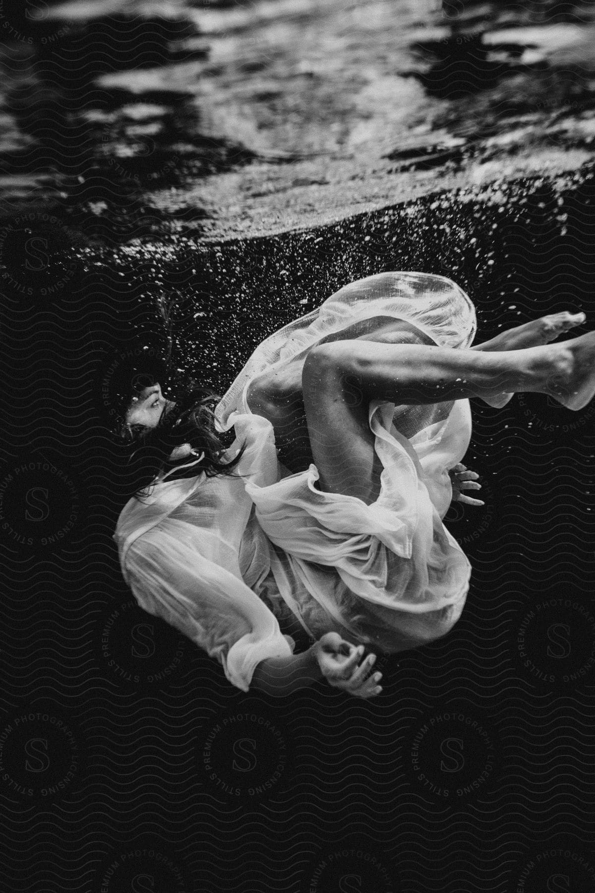 A woman floating underwater near the surface her dress exposing her legs