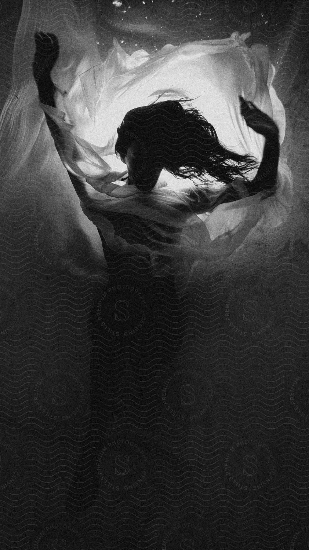 A black and white photograph of a woman gracefully submerged in water her flowing dress creating a mesmerizing contrast