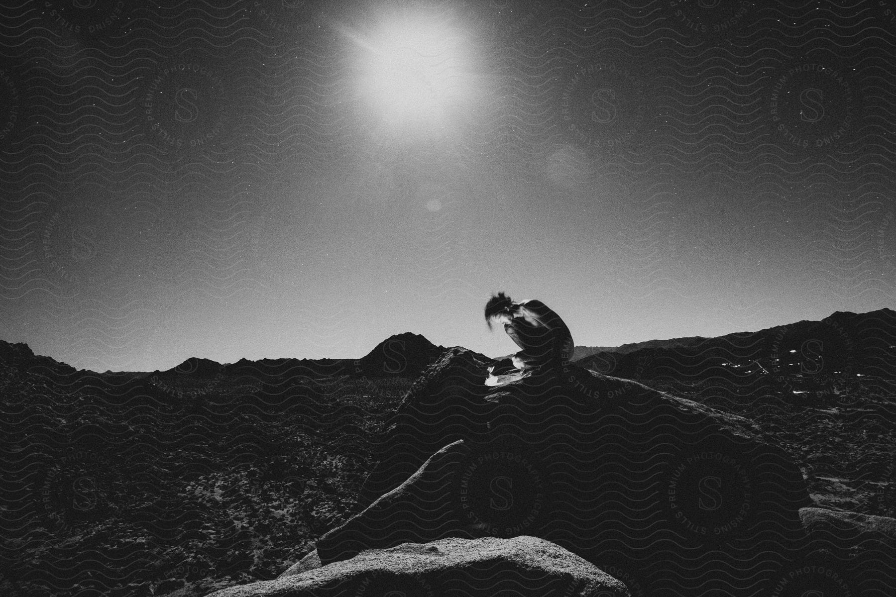 Stock photo of person squatting in front of a small fire outdoors on top of a big rock