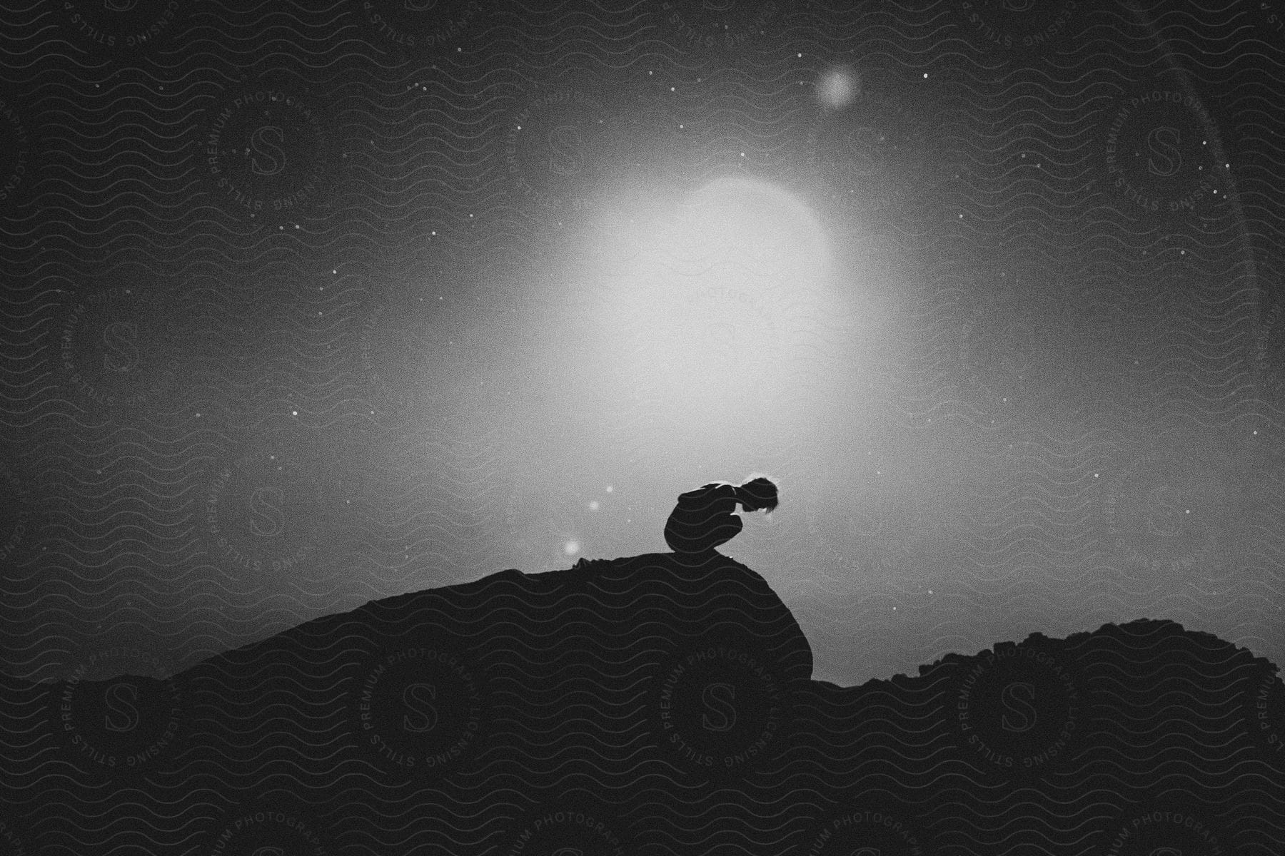 A man kneels on top of a mountain at night