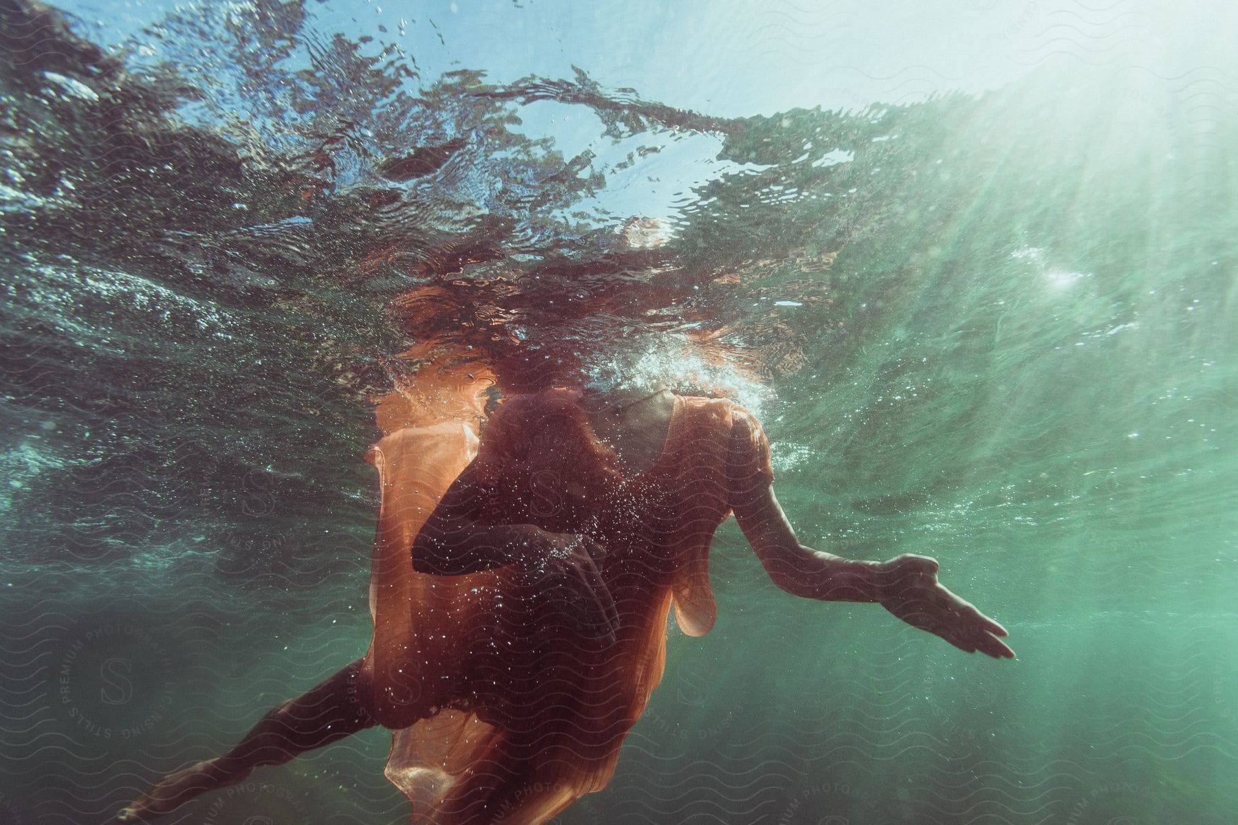 A woman in a meloncolored dress wades in water with her head above while her body is under water