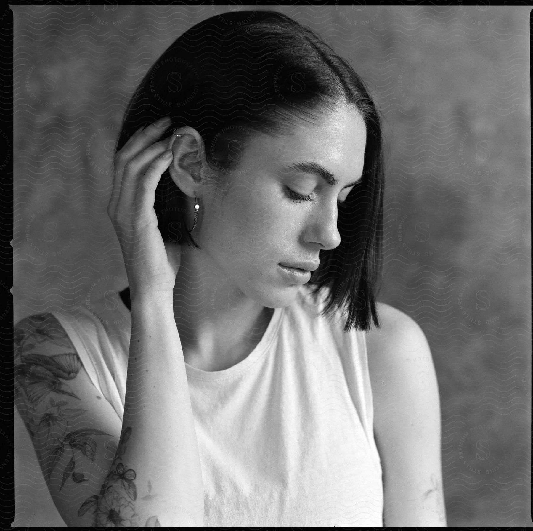 A young woman with tattoos brushes her hair behind her ear