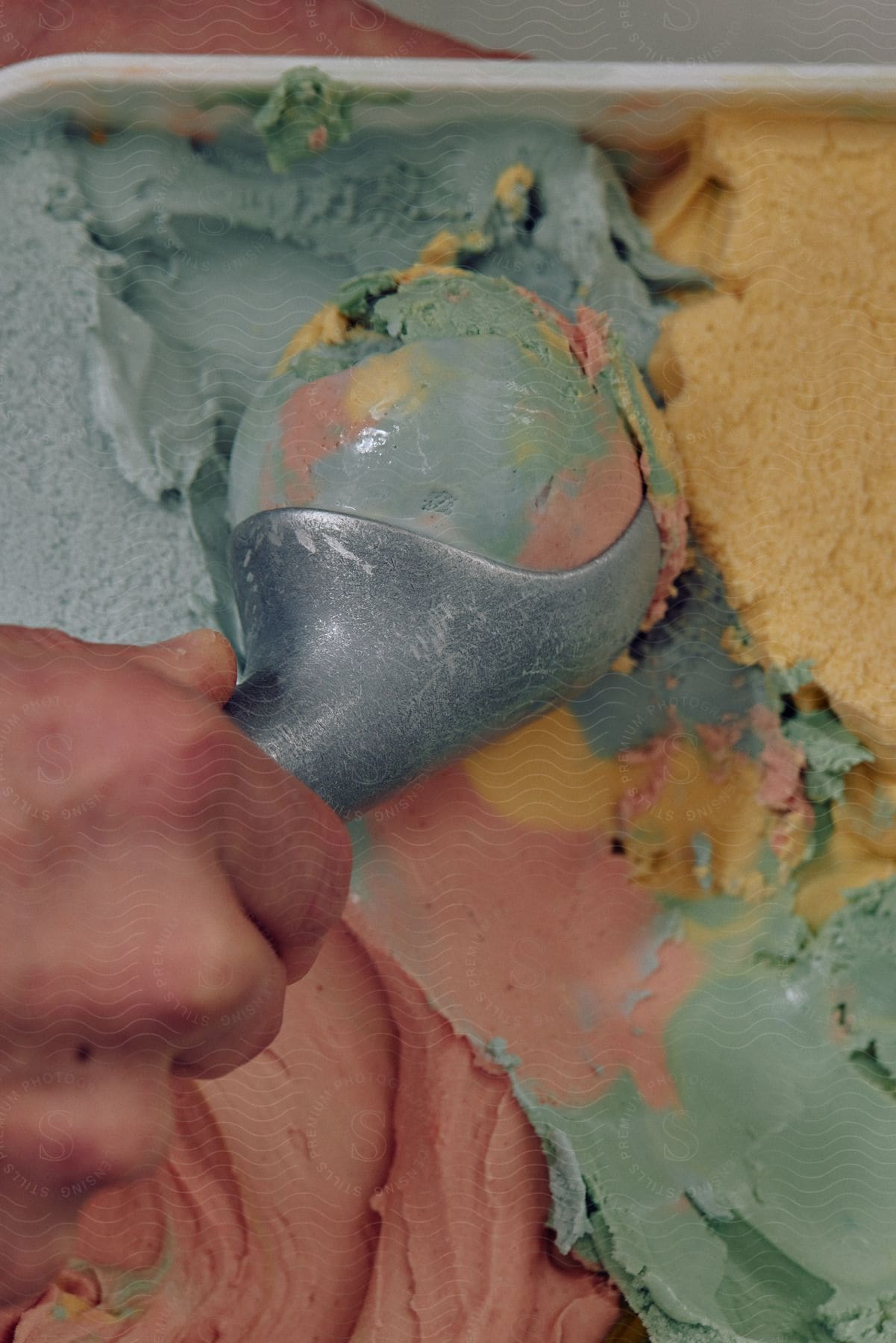 A Hand Scooping Up Rainbowcolored Ice Cream Using An Ice Cream Scoop