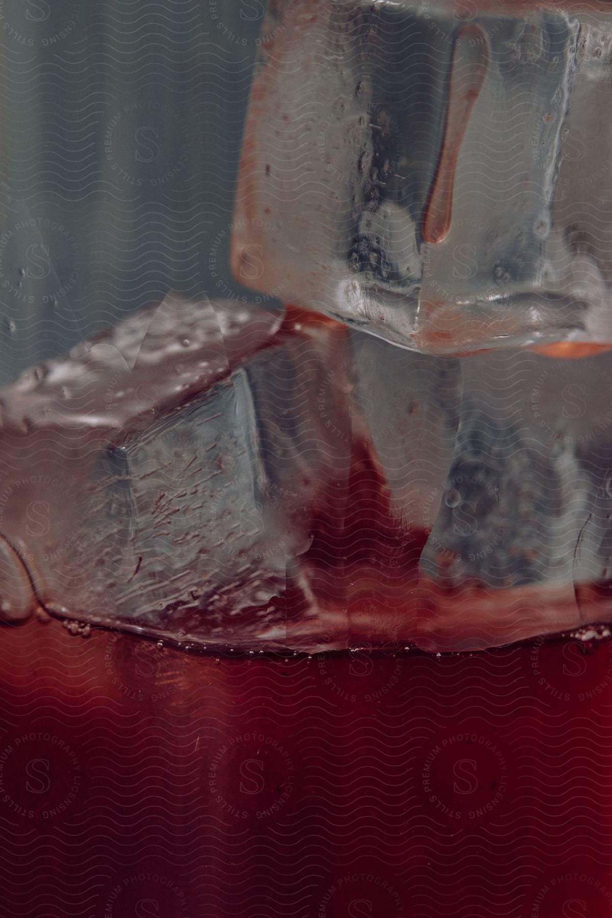 A cup with ice cubes and a red drink inside