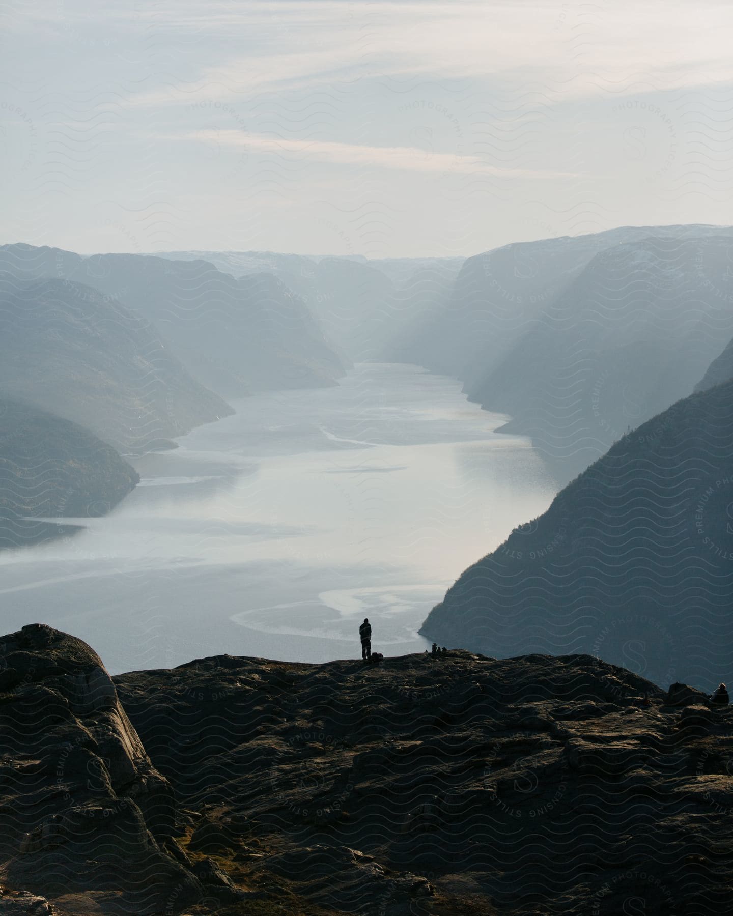 A man stands on the edge of a cliff overlooking a fjord