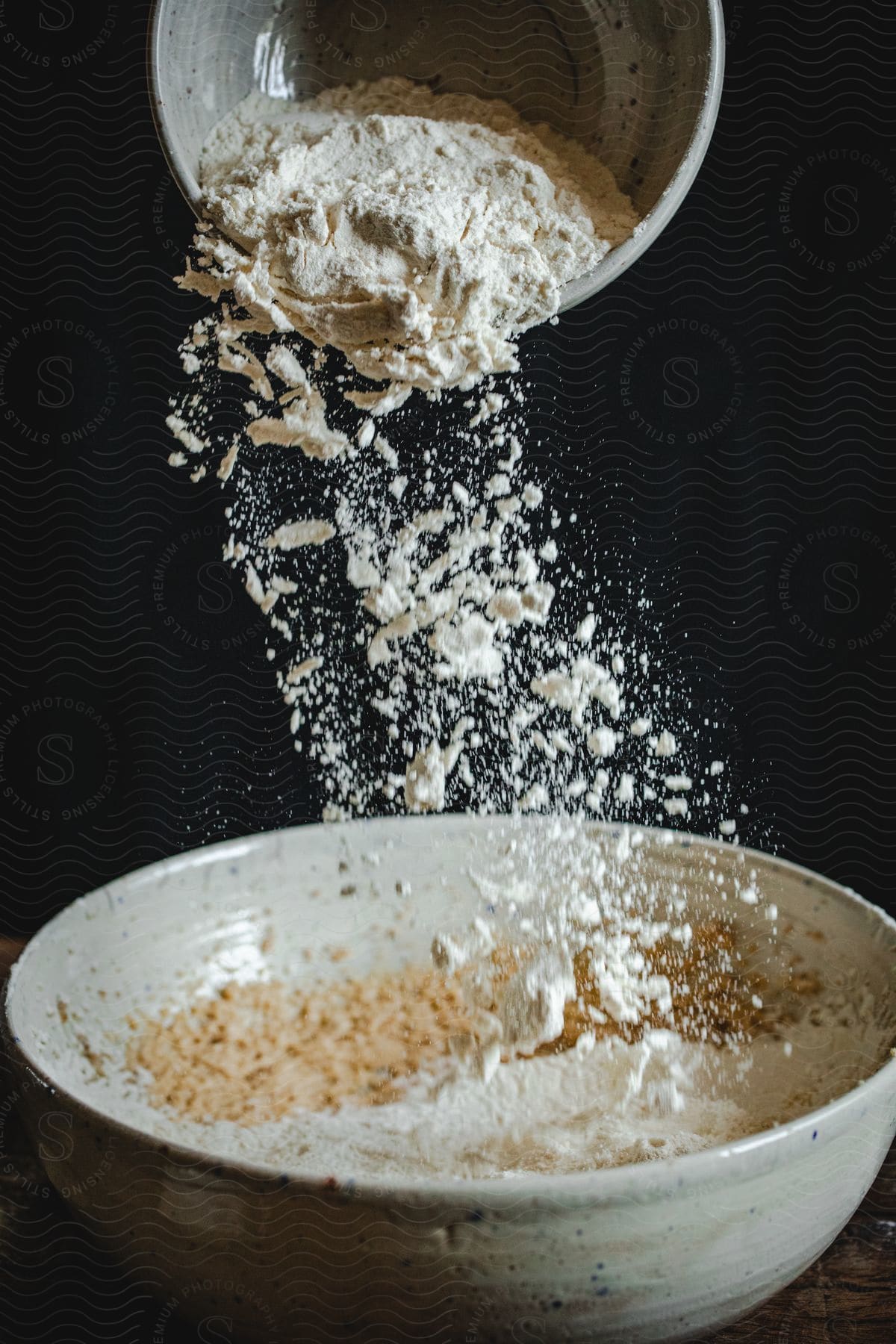 Flour sifts from a smaller ceramic bowl into a larger ceramic bowl