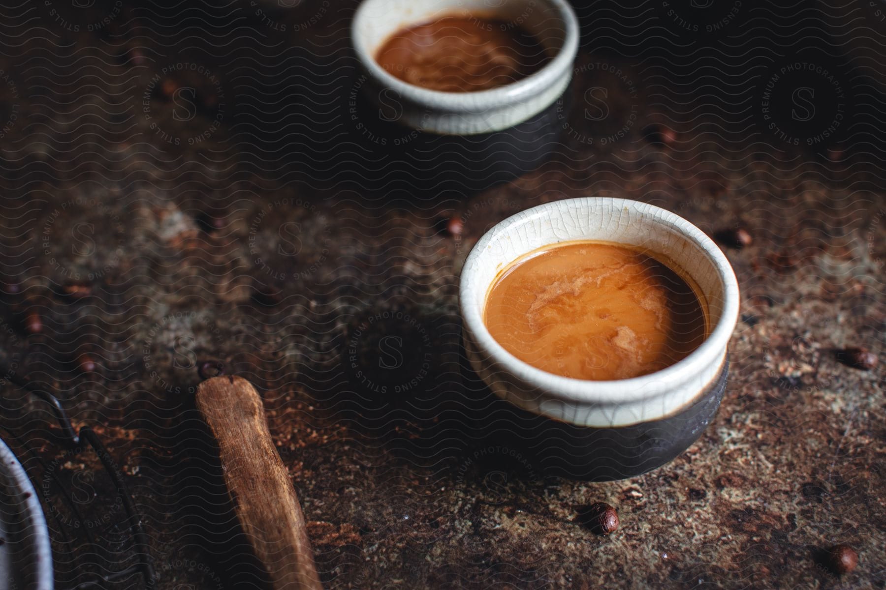 A Stone Table With Two Bowls Of Brown Liquid A Wooden Tool Handle And Scattered Brown Beans