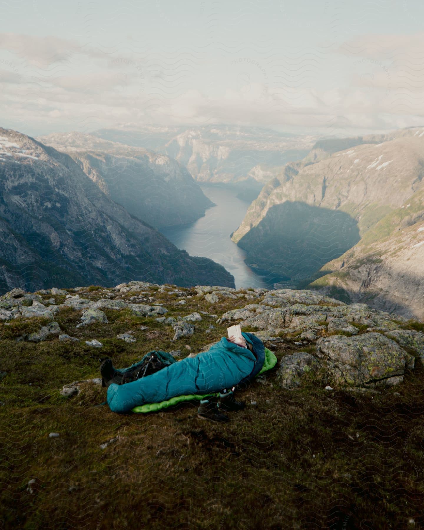 A person is in a sleeping bag near a canyon cliff over a river in nature