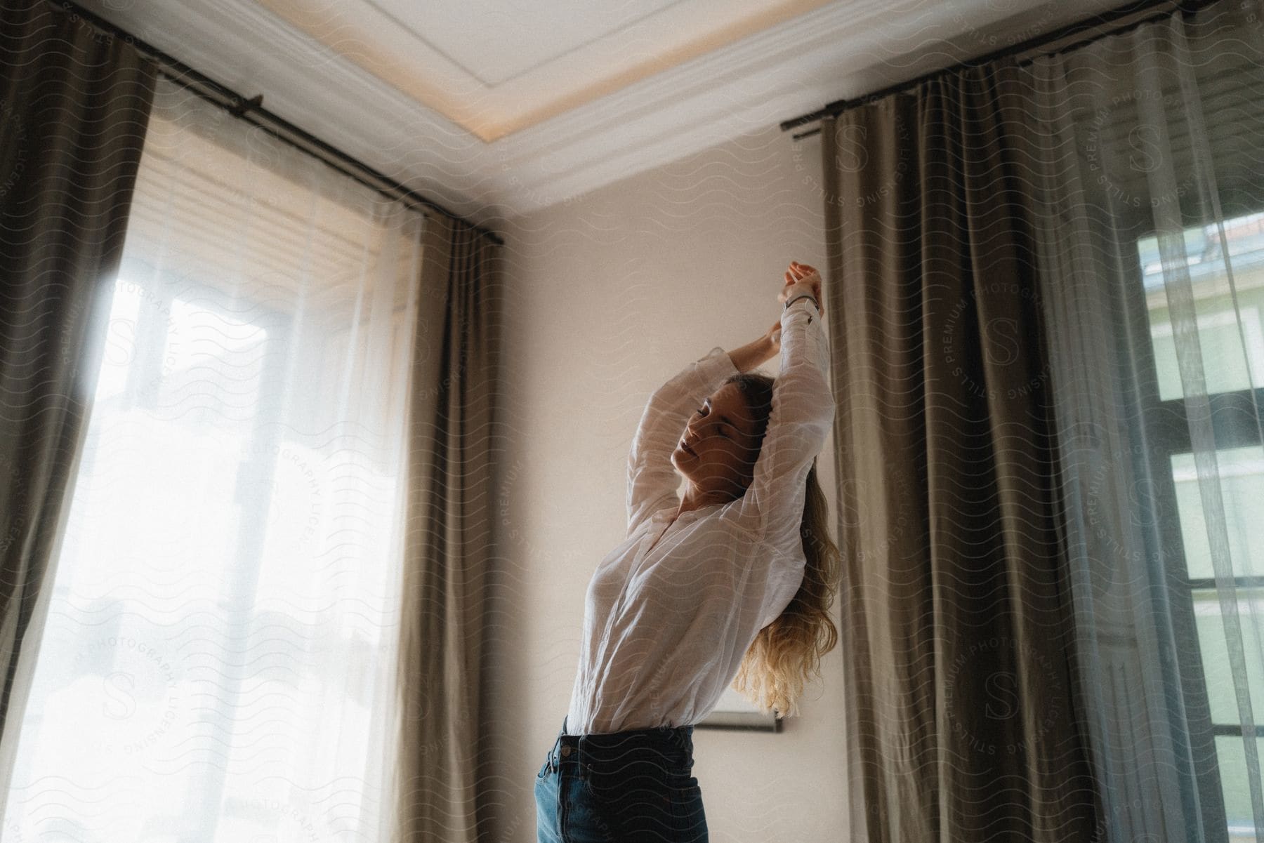 A woman in a white shirt lifting her arms up in a living room