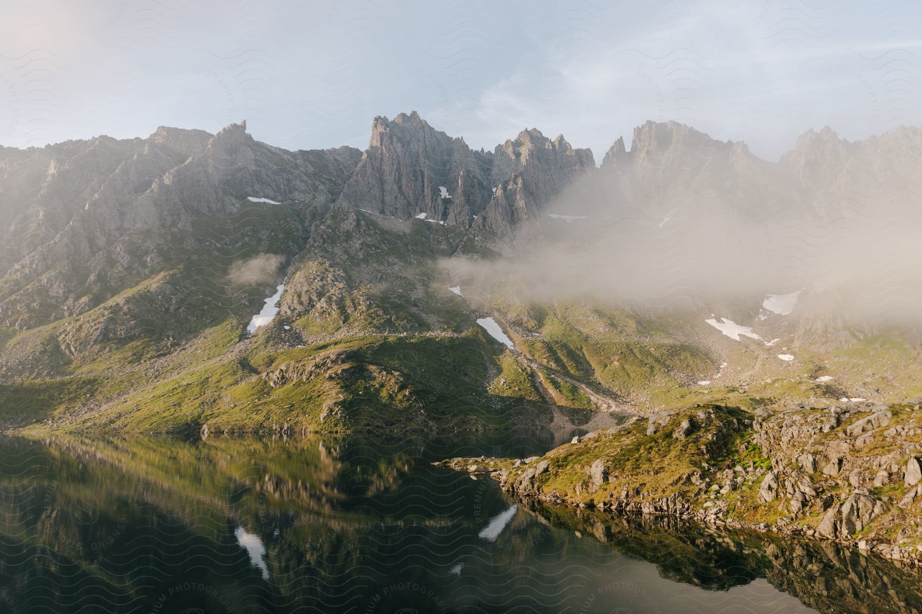 A serene view of a mountain range reflected in a calm lake surrounded by lush vegetation