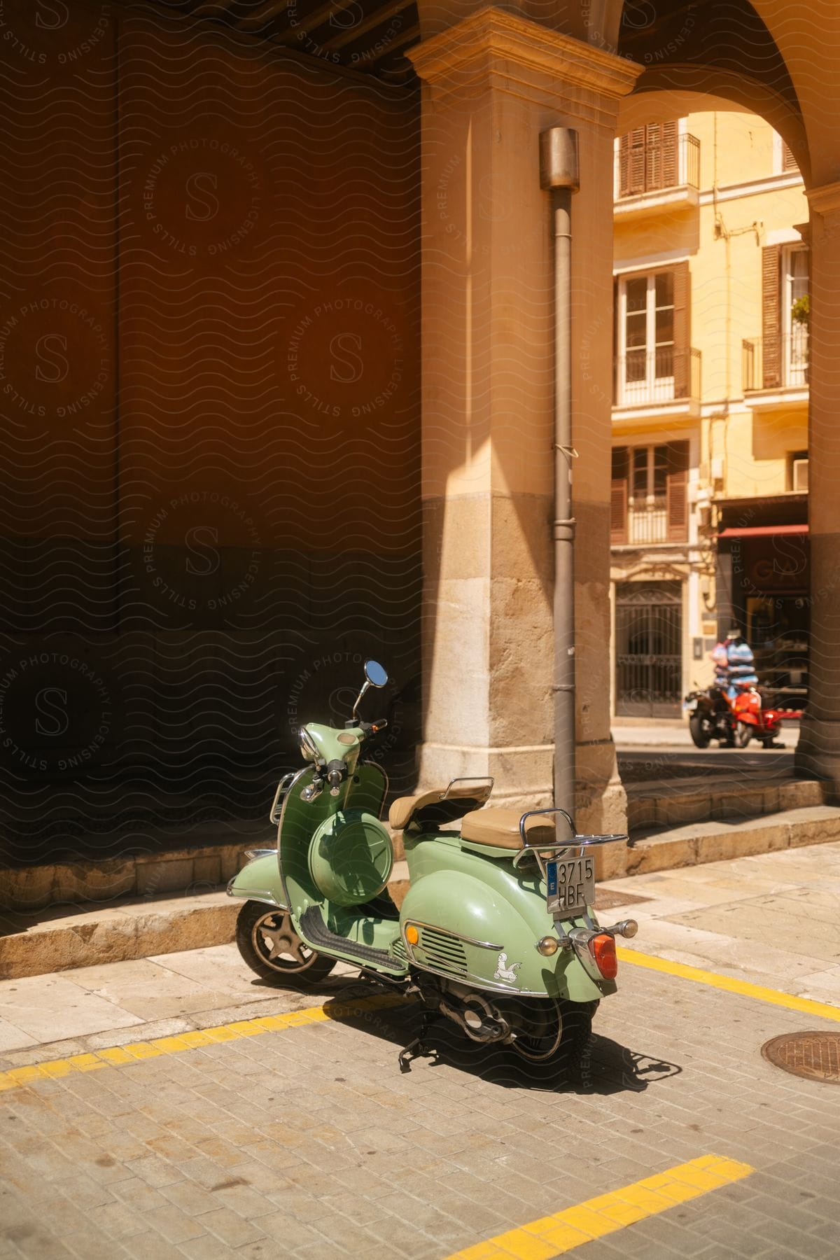 An old green motorcycle parked near a building with arches in a city