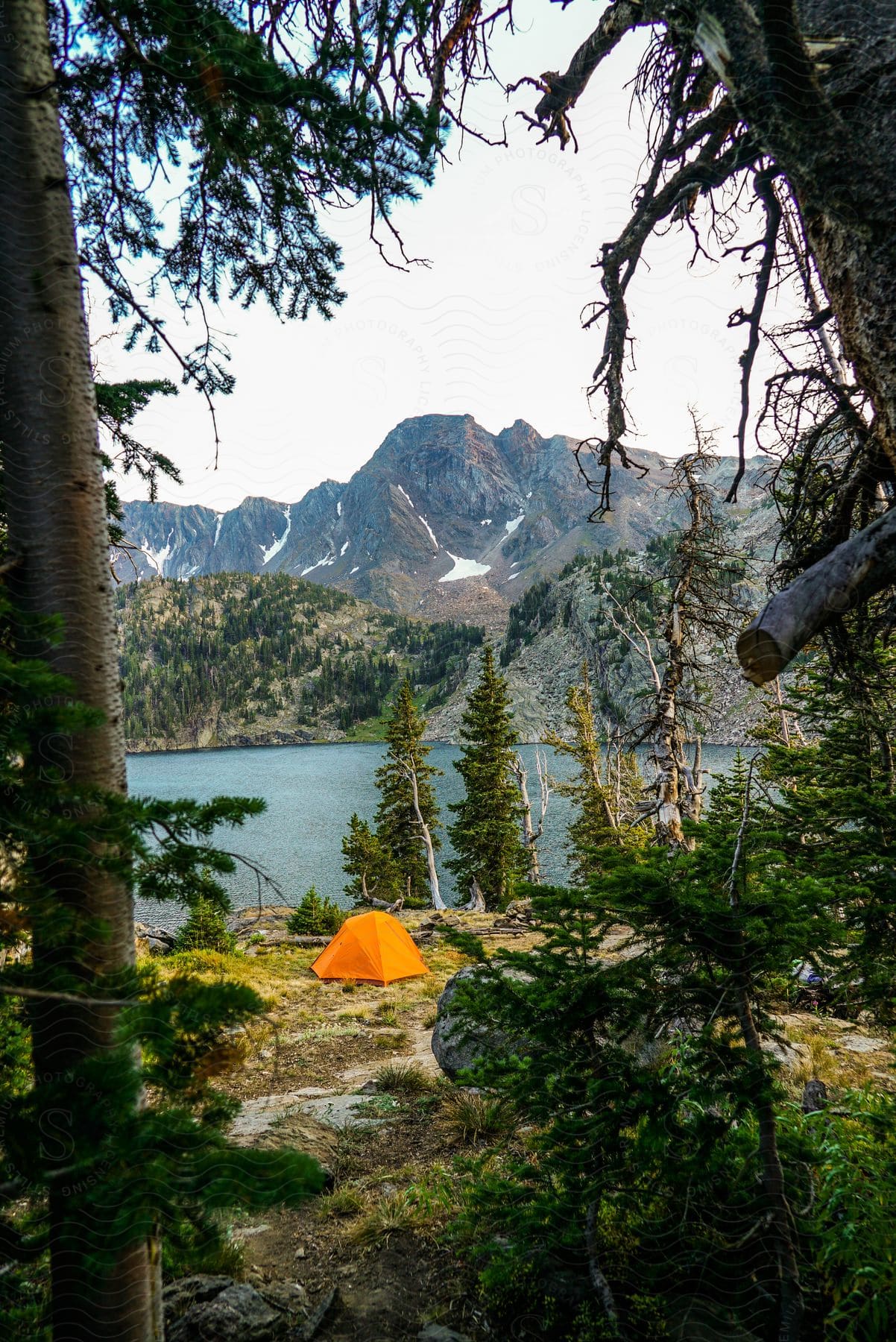 An orange tent pitched near a lake and a rocky peak in the mountains