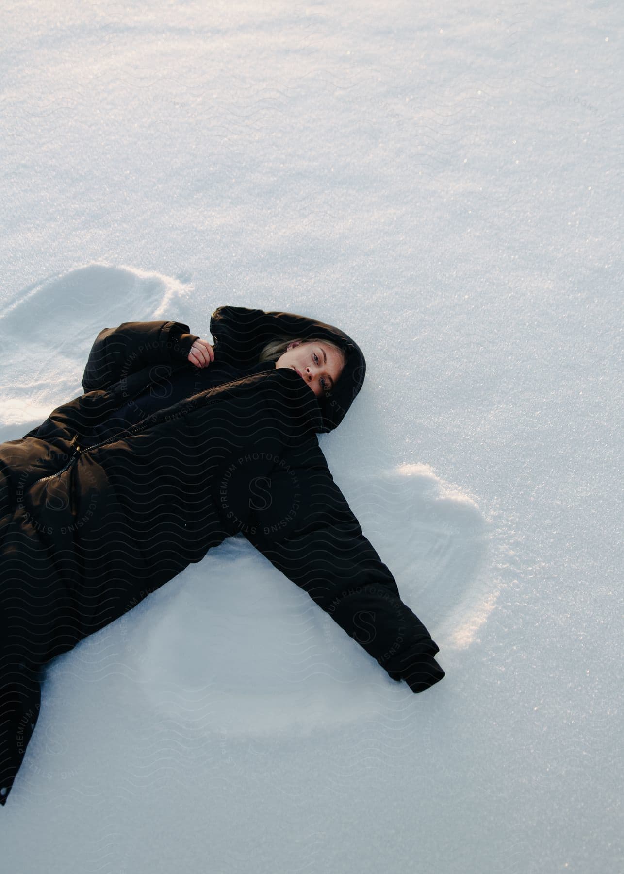 Young woman wearing a thick winter coat making snow angels at evening