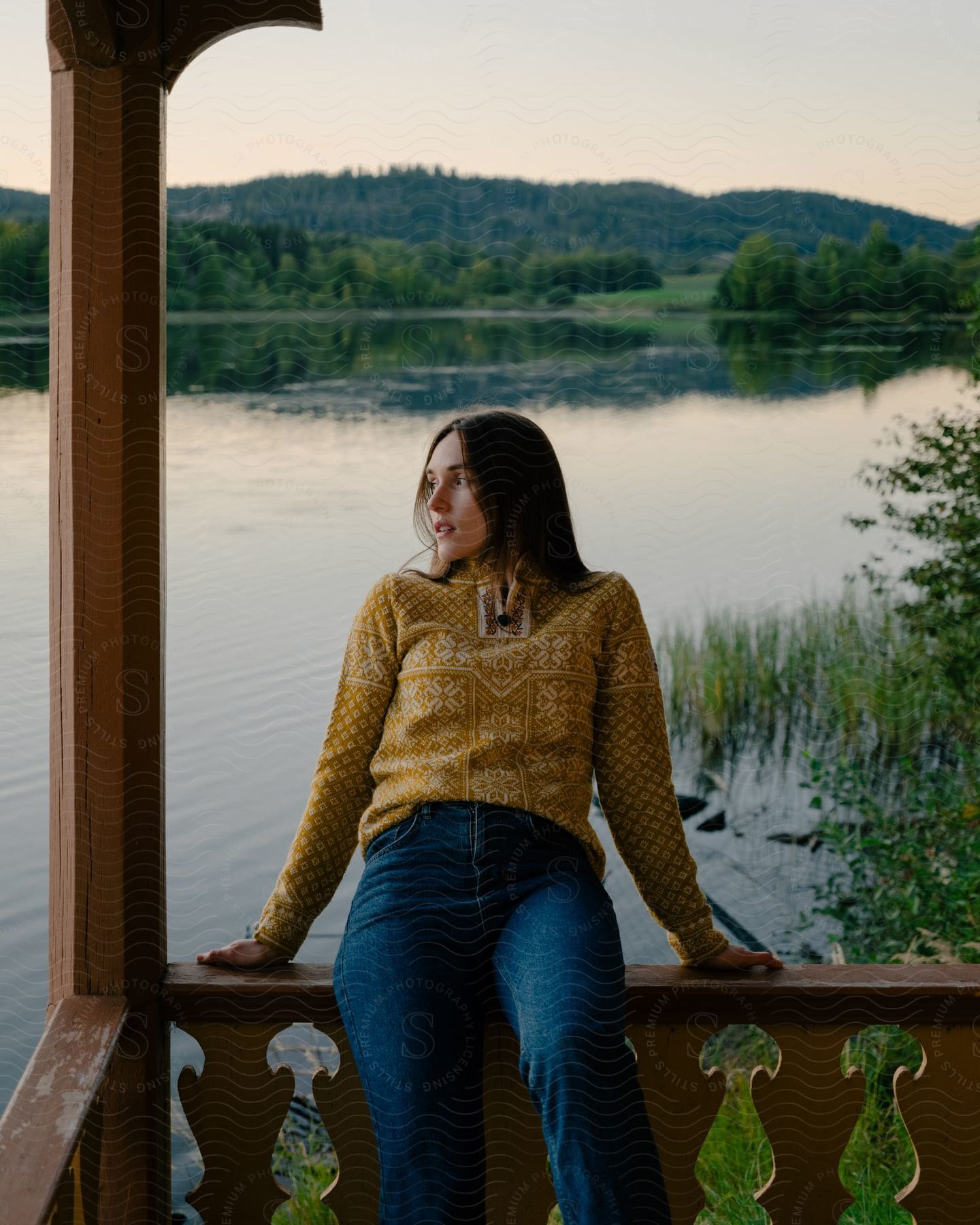 A woman posing outdoors in front of a lake sitting on a railing