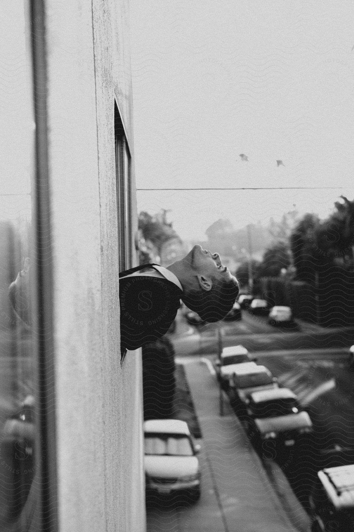 A man in a suit leans out of an office window in a city setting